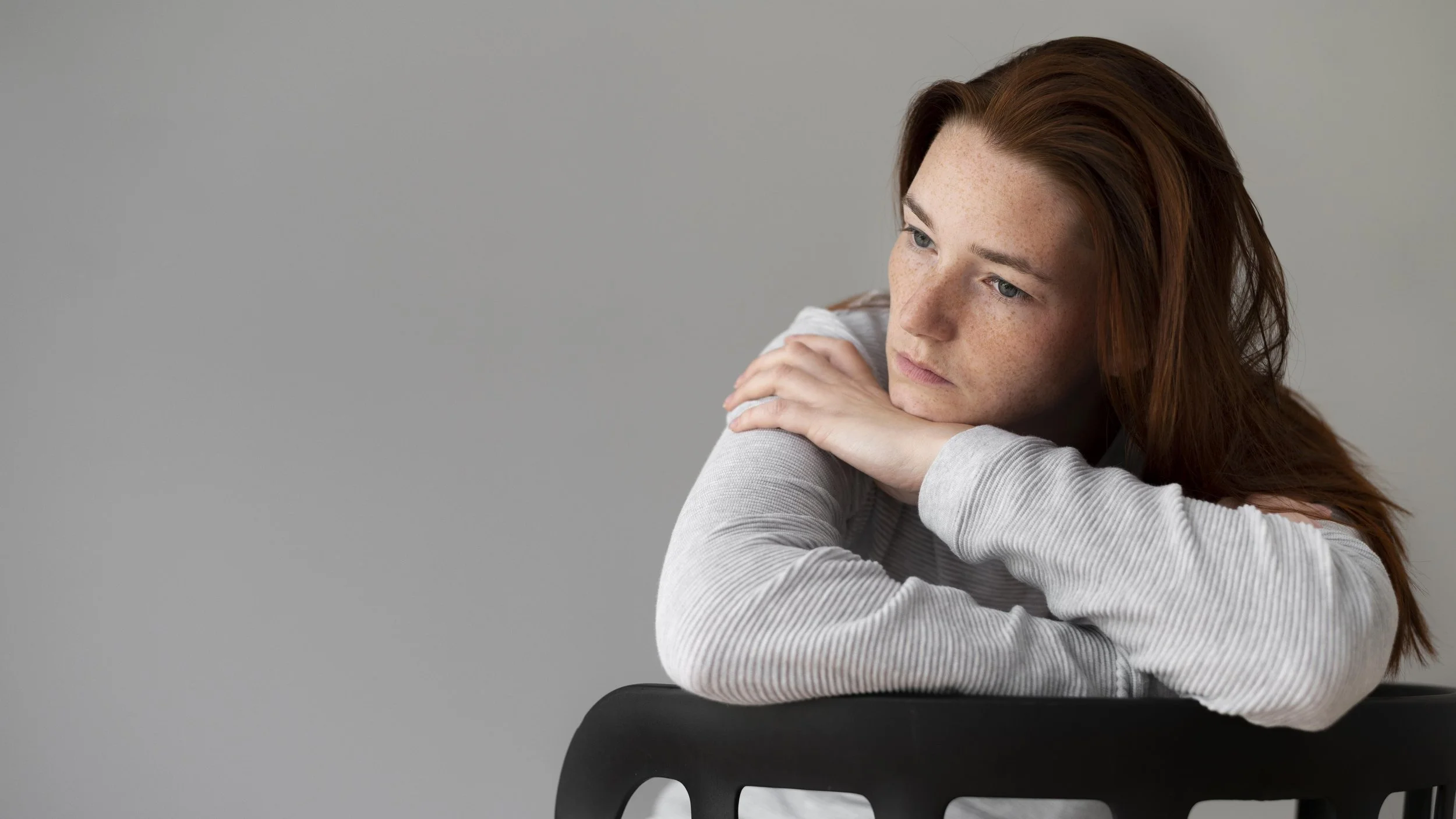 A woman looking away from a distance while sitting on a chair - Calm Harbor Counseling