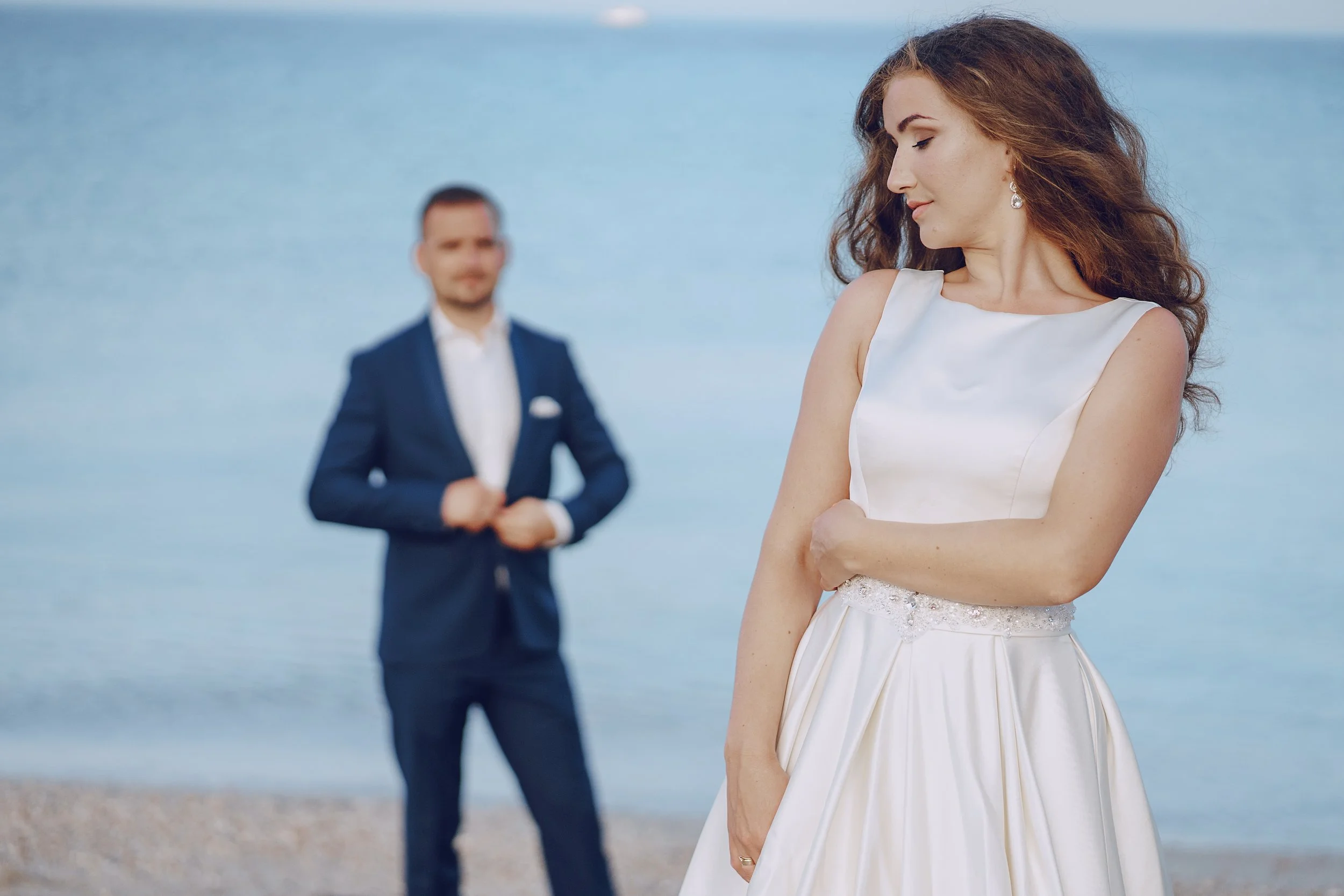 A wedding photoshoot on a beach with the groom away from the bride - Calm Harbor Counseling