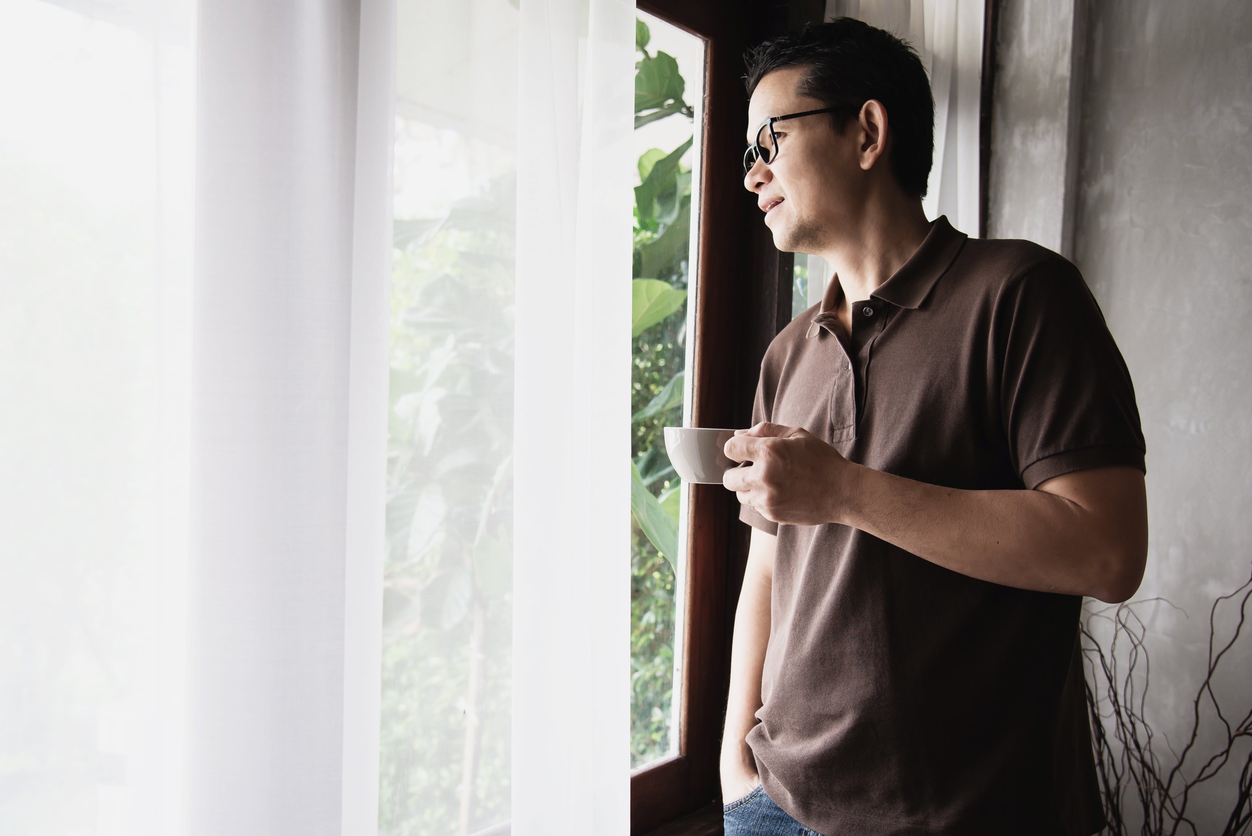 A man drinking coffee while looking outside a window - Calm Harbor Counseling