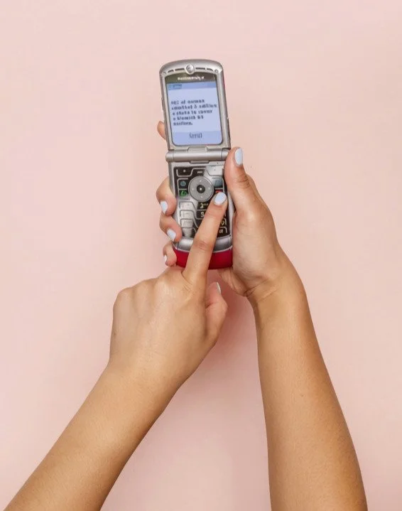 Person holding a silver flip phone with a blue screen against a pink background.