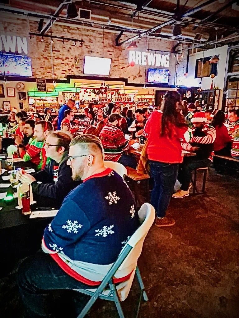 “Group of singles seated and socializing together during a large in-person dating event at a brewery.