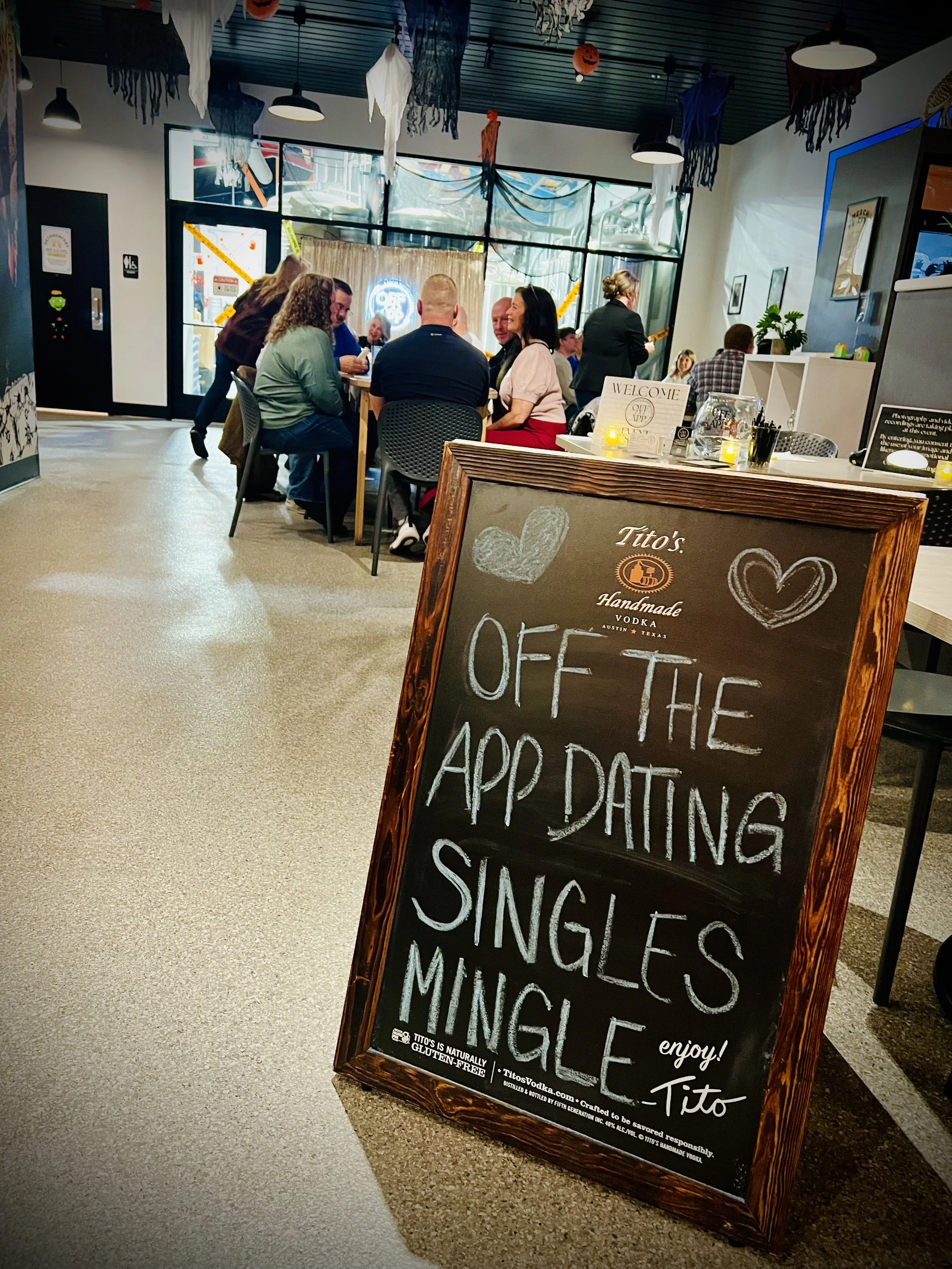 Chalkboard sign reading ‘Off The App Dating Singles Mingle’ displayed inside a venue during a social event hosted at Cocoon Brewing Company in De Pere, WI