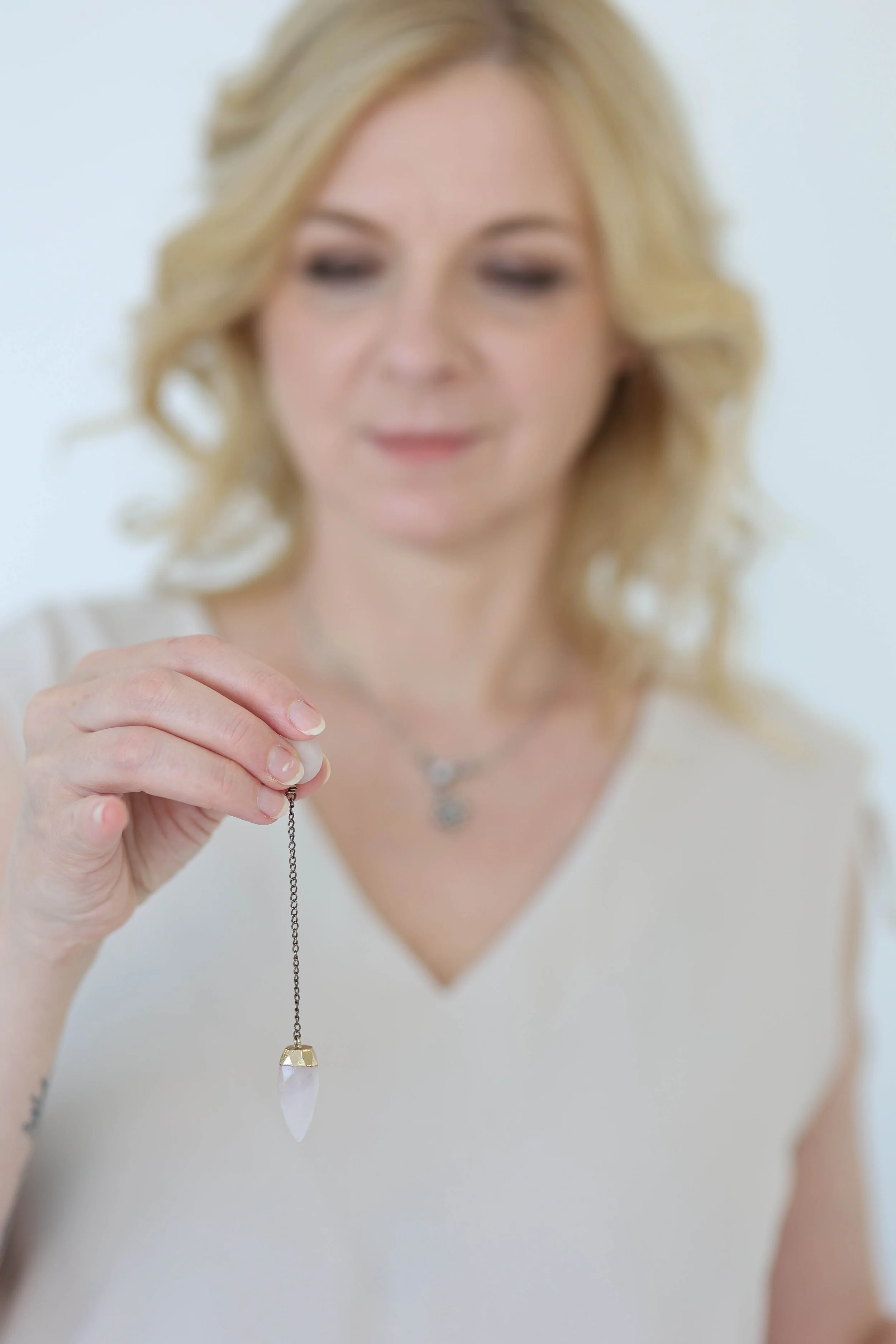 Woman holding a necklace with a pointed, crystal pendant