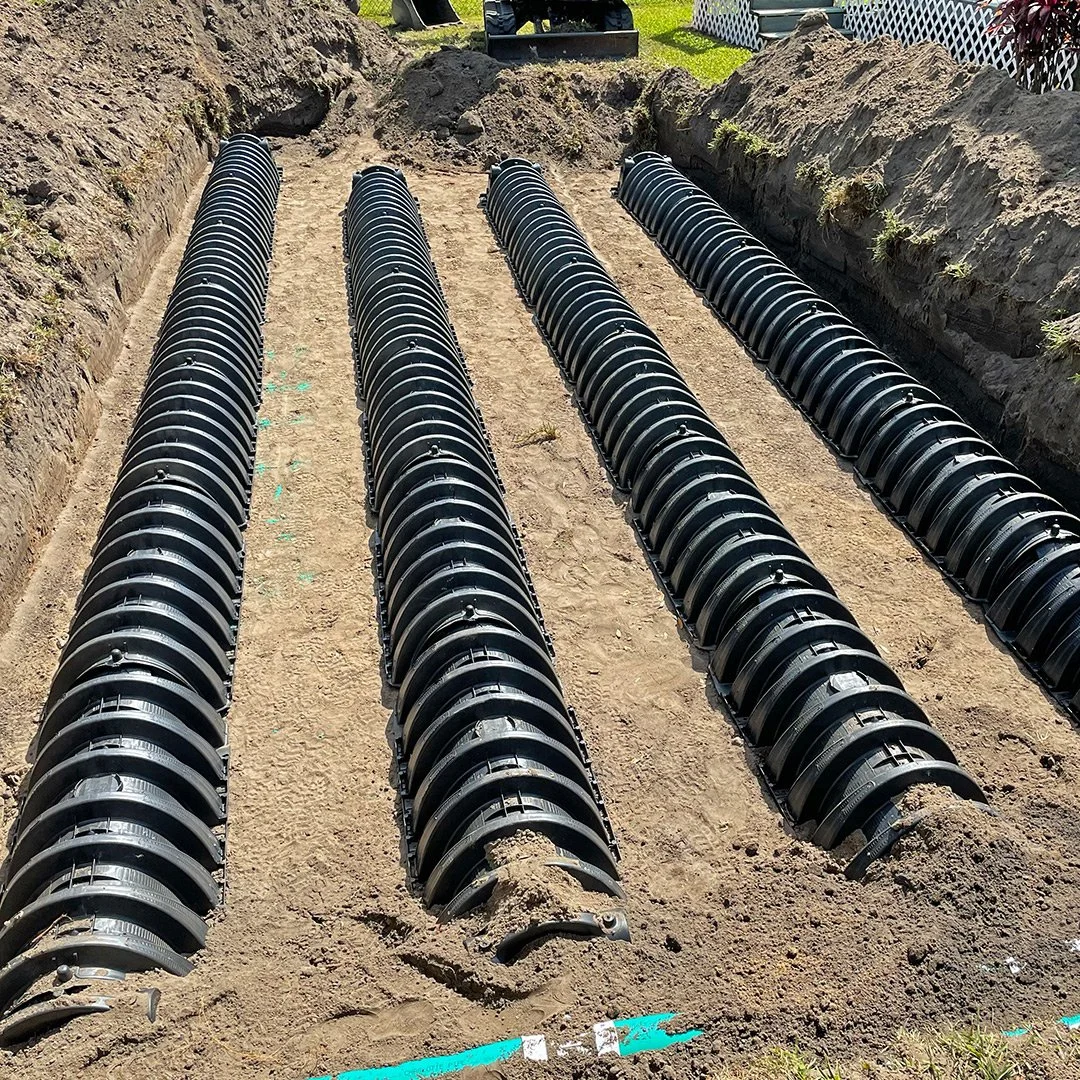 Four rows of large black underground drainage pipes installed in a prepared trench.