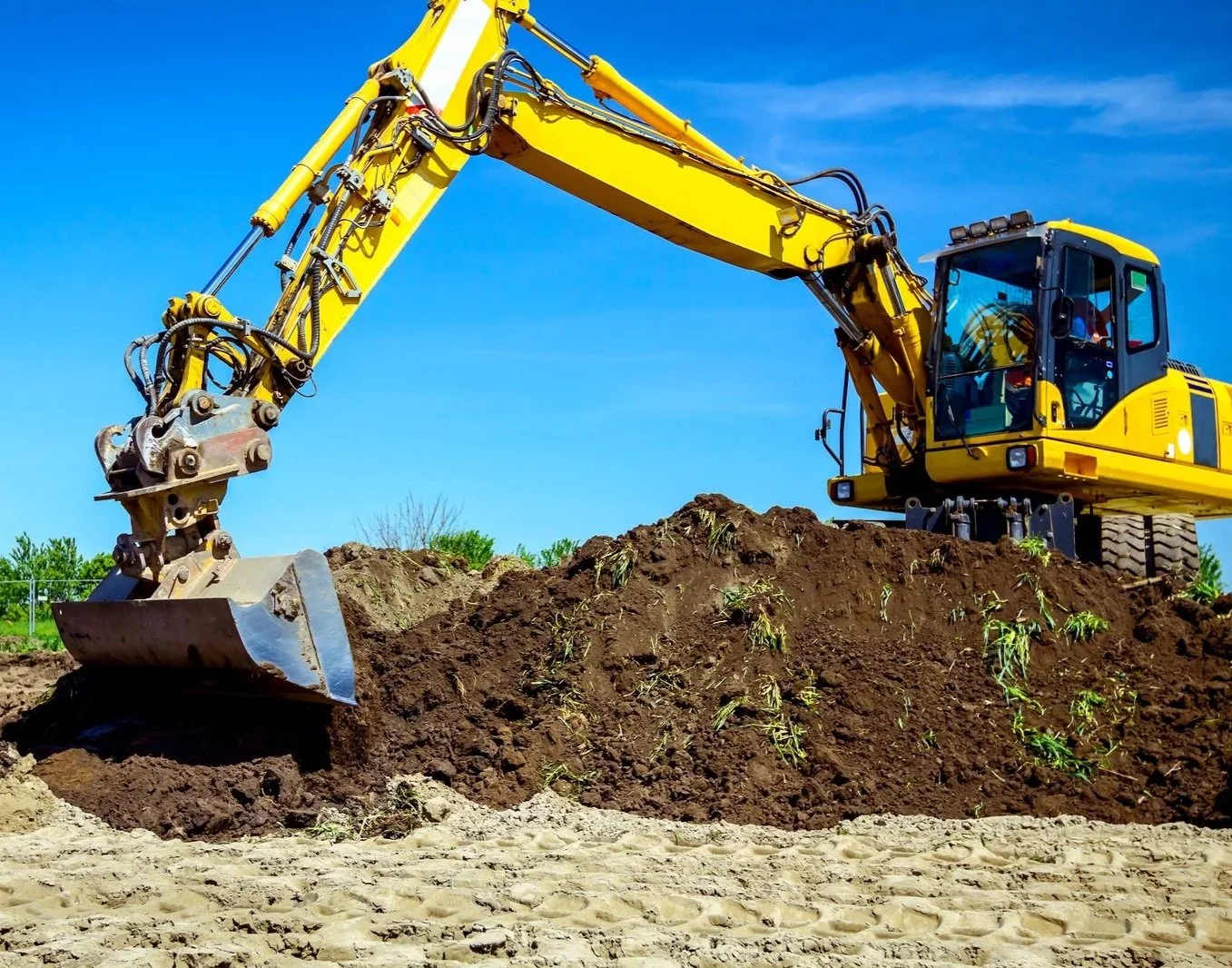Yellow excavator digging into a mound of dirt on a construction site under a blue sky.