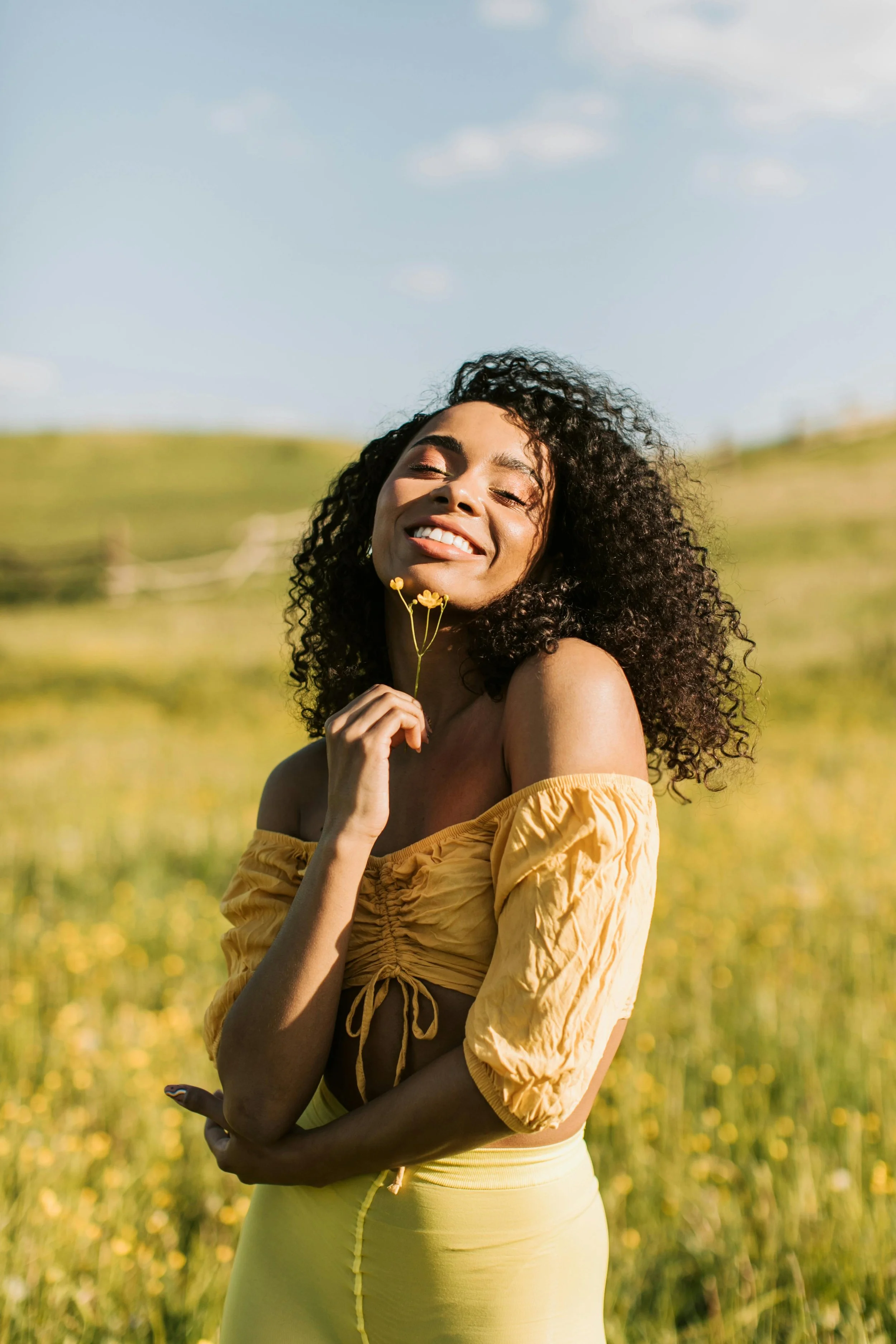 Woman in a meadow wearing a yellow two piece outfit, smiling , holding a small flower experiencing relief from virtual therapy for adult women with ADHD in south carolina and arizona