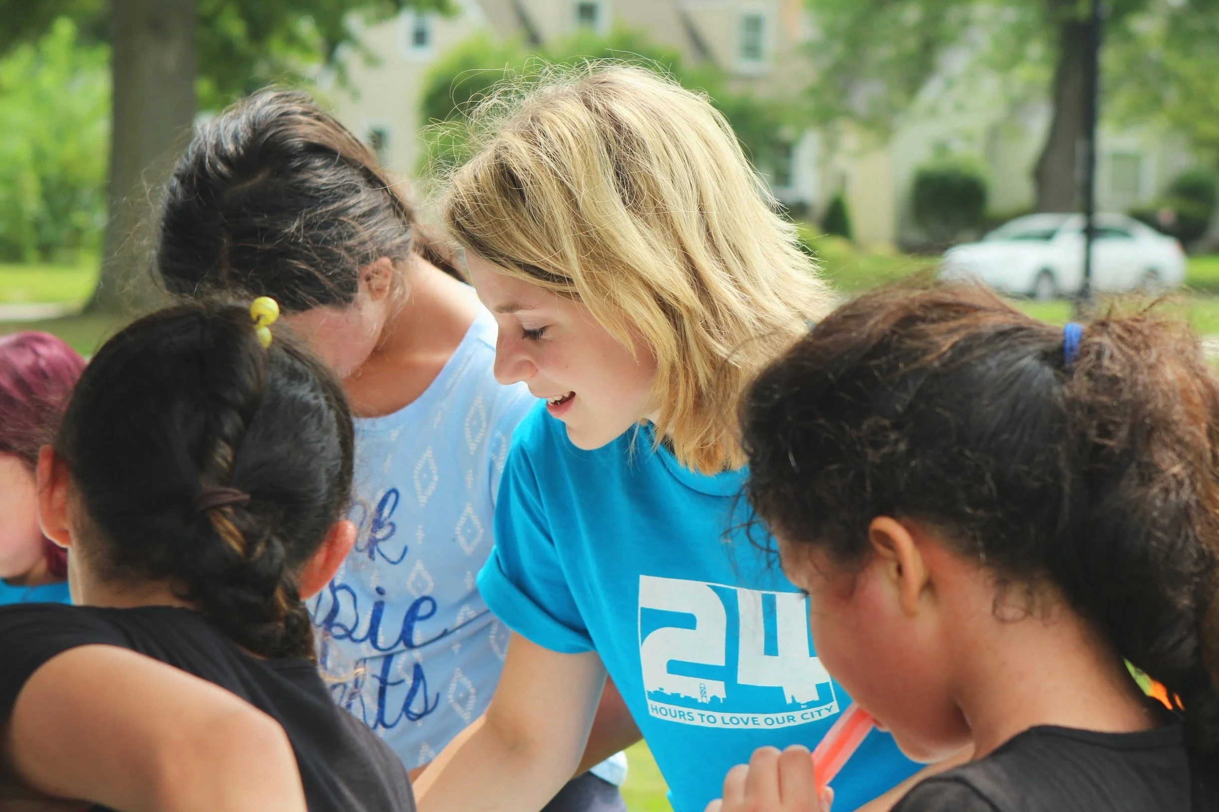 Group of women and girls outdoors, standing close together, smiling and engaging with each other.