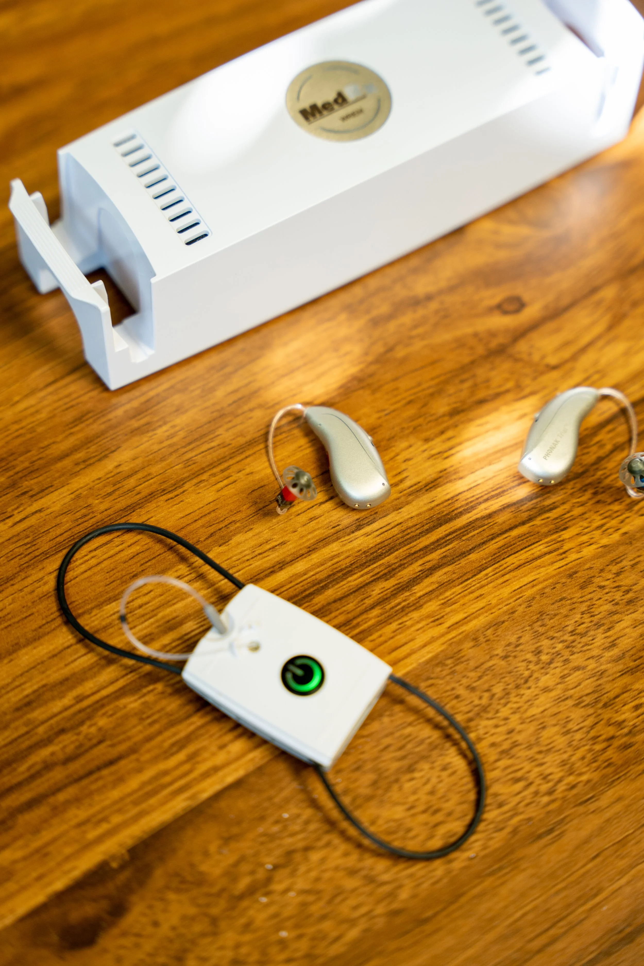 Hearing Aid Programming Device called Real Ear Measures pictured with hearing aids on a wooden desk.