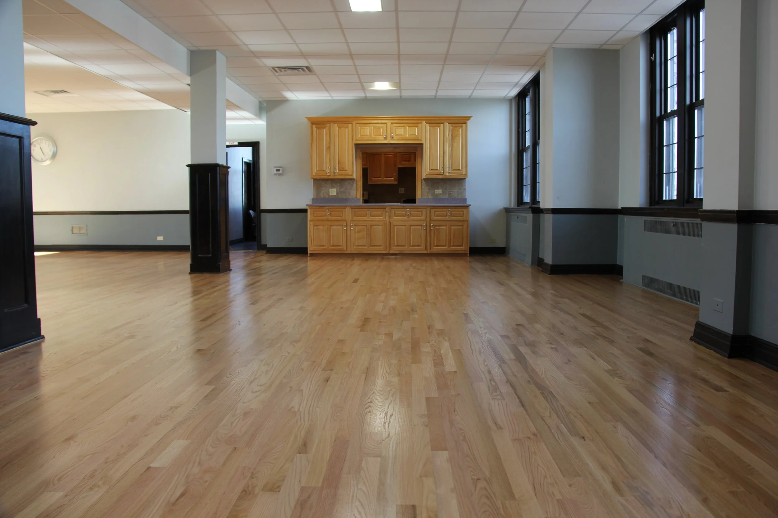 Empty room with hardwood floors, large windows, and a built-in wooden cabinet.