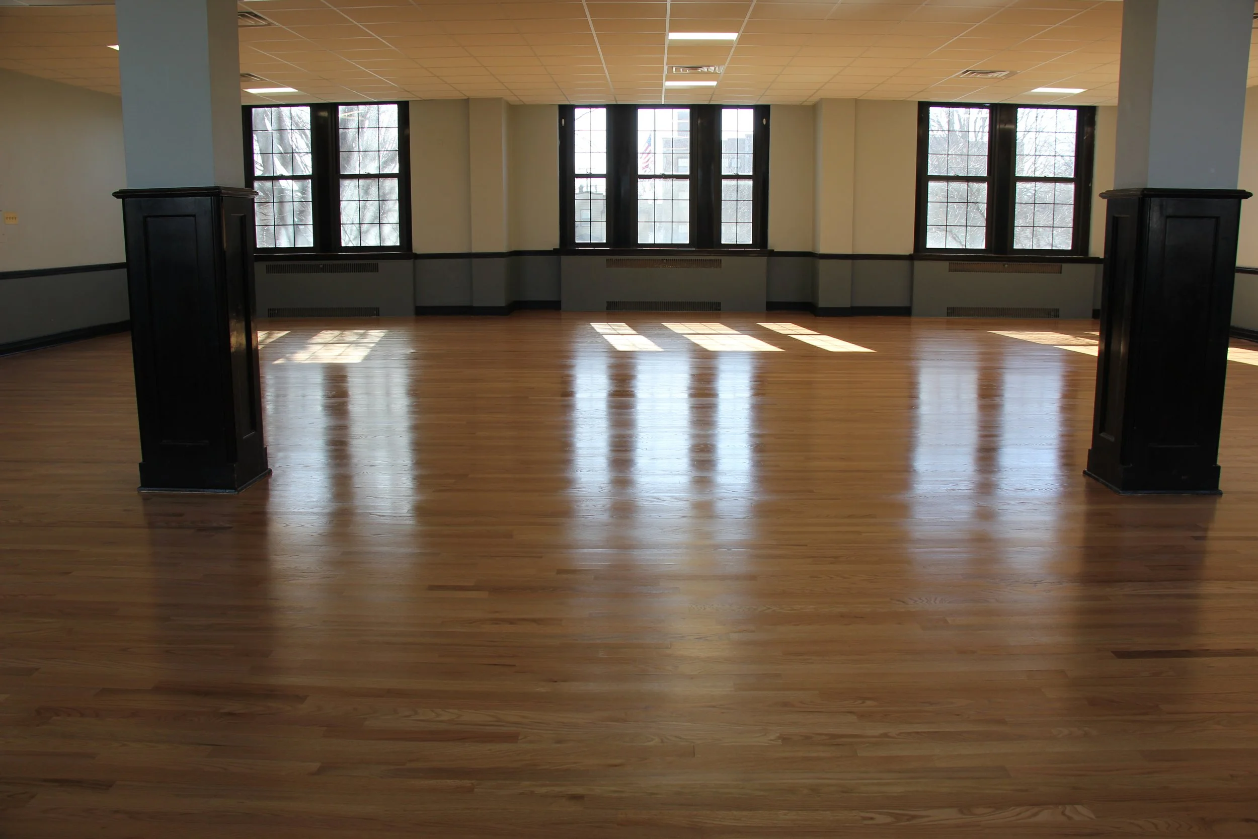 Empty room with large windows, wooden floor, light-colored walls, and black column supports.