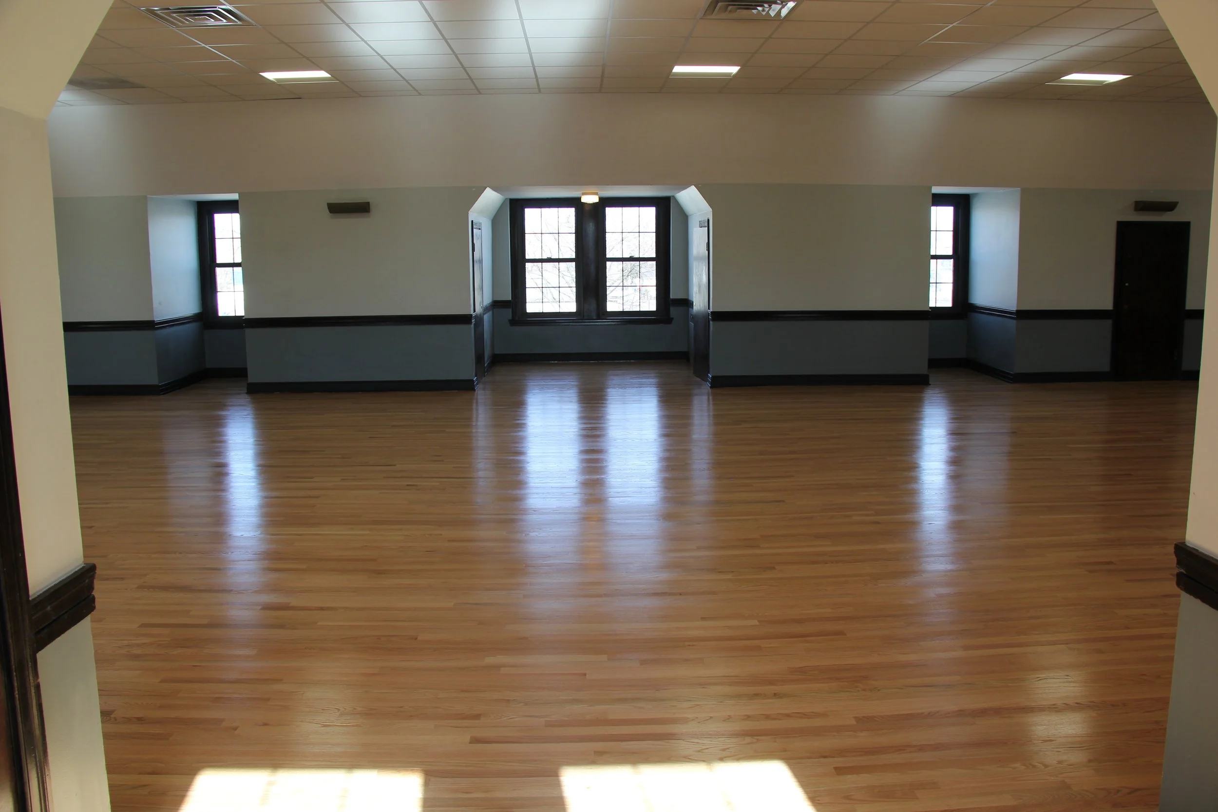 Empty room with hardwood floors, white walls, and windows letting in natural light.