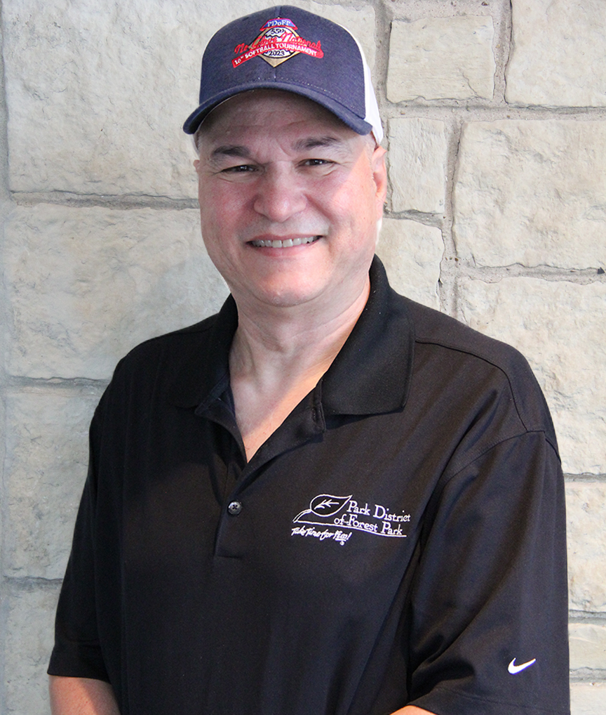 A man wearing a navy baseball cap with red and white embroidery, a black polo shirt with a logo and text on the left chest, and standing in front of a stone wall.