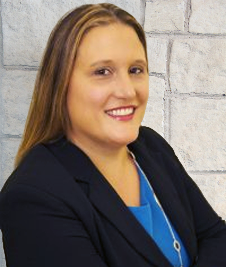 Portrait of a woman with long, light brown hair, smiling, in front of a beige brick wall, wearing a black blazer and blue top.