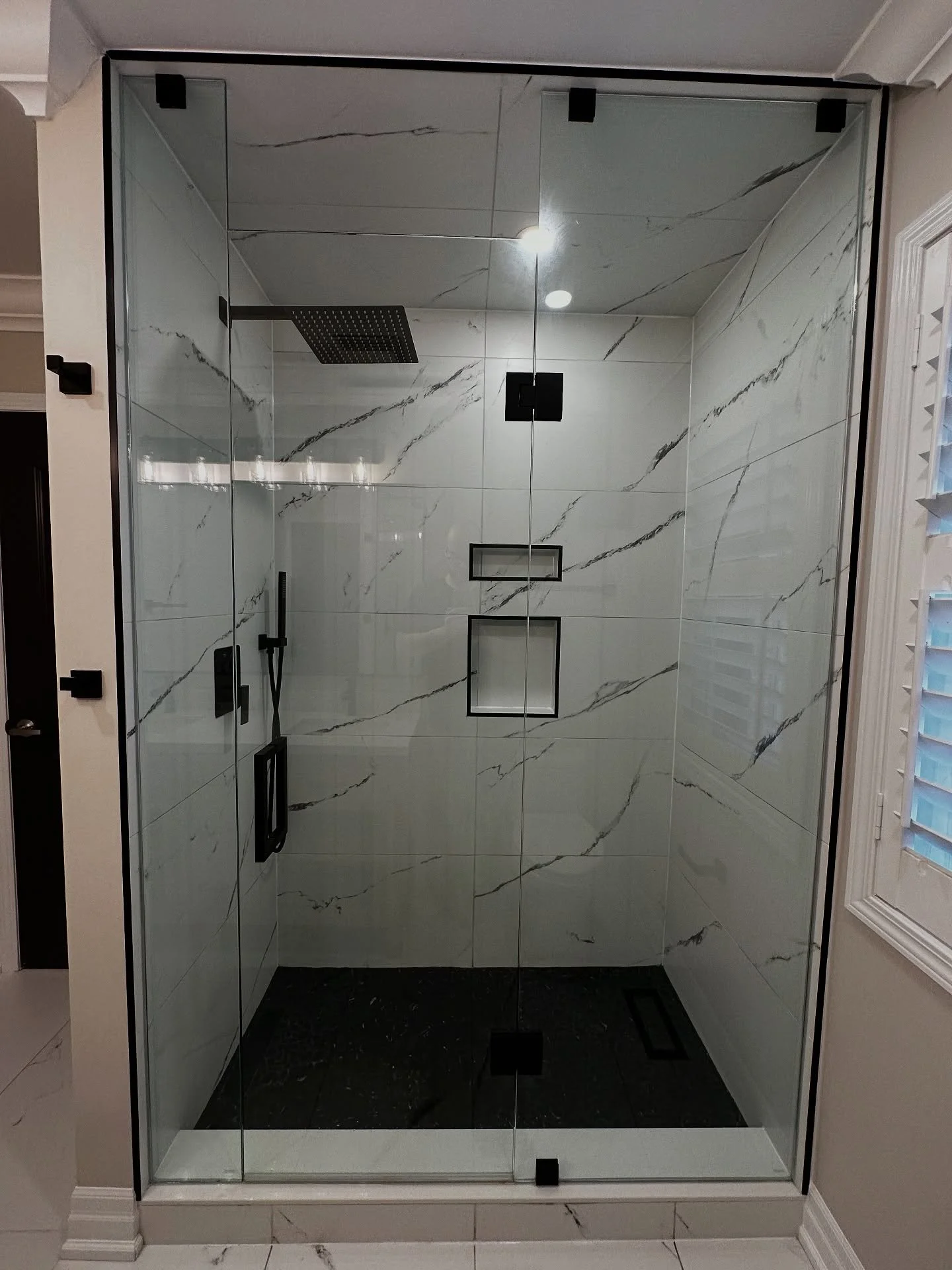 ✨ From outdated to outstanding ✨
Check out this stunning transformation &ndash; a sleek glass shower with bold black fixtures, large-format marble look tiles, built-in niches, and a modern rainfall showerhead.

This space is now pure luxury, blending