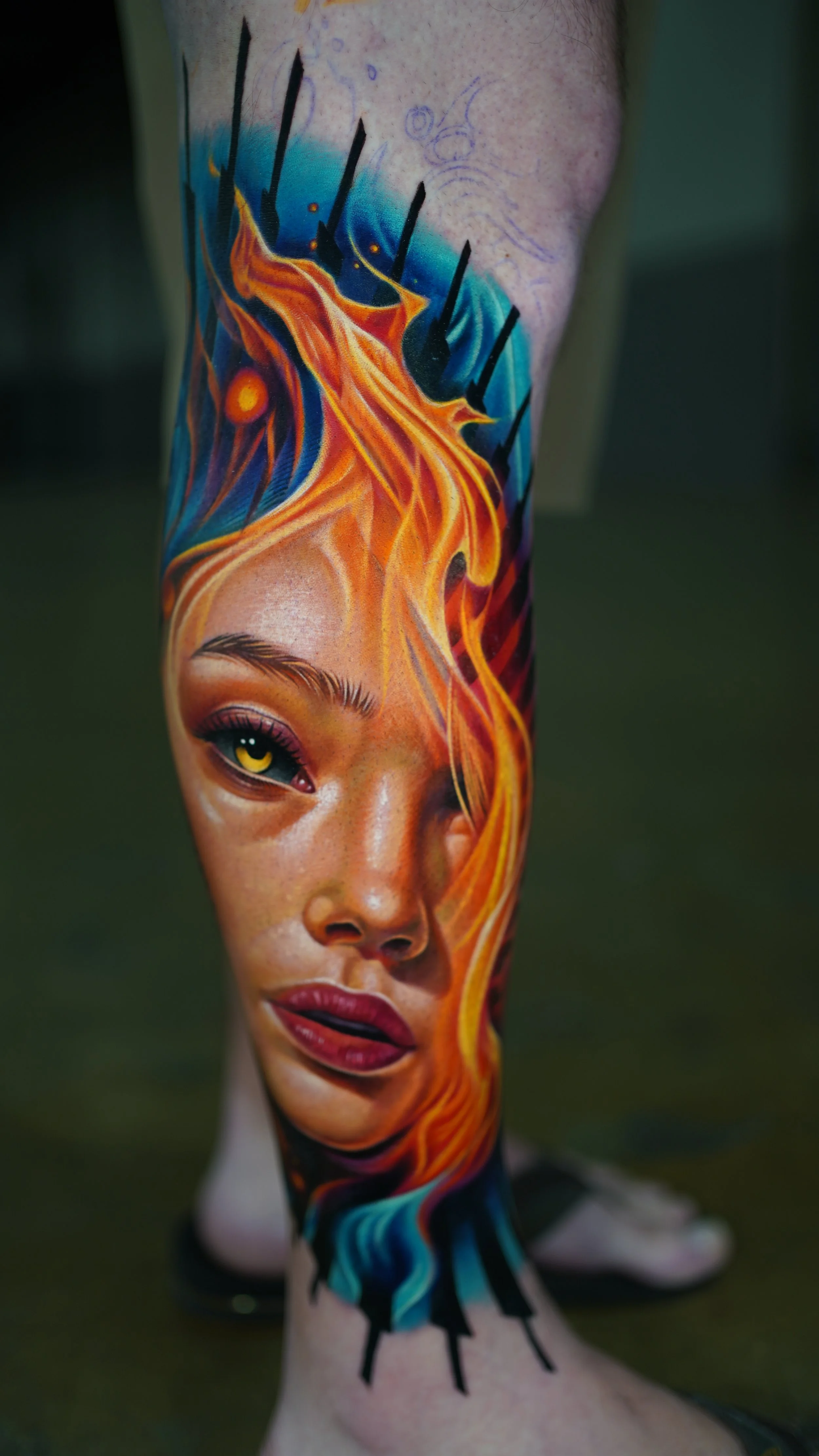 Colorful tattoo of a woman's face with fiery orange and red hair on a person's leg.