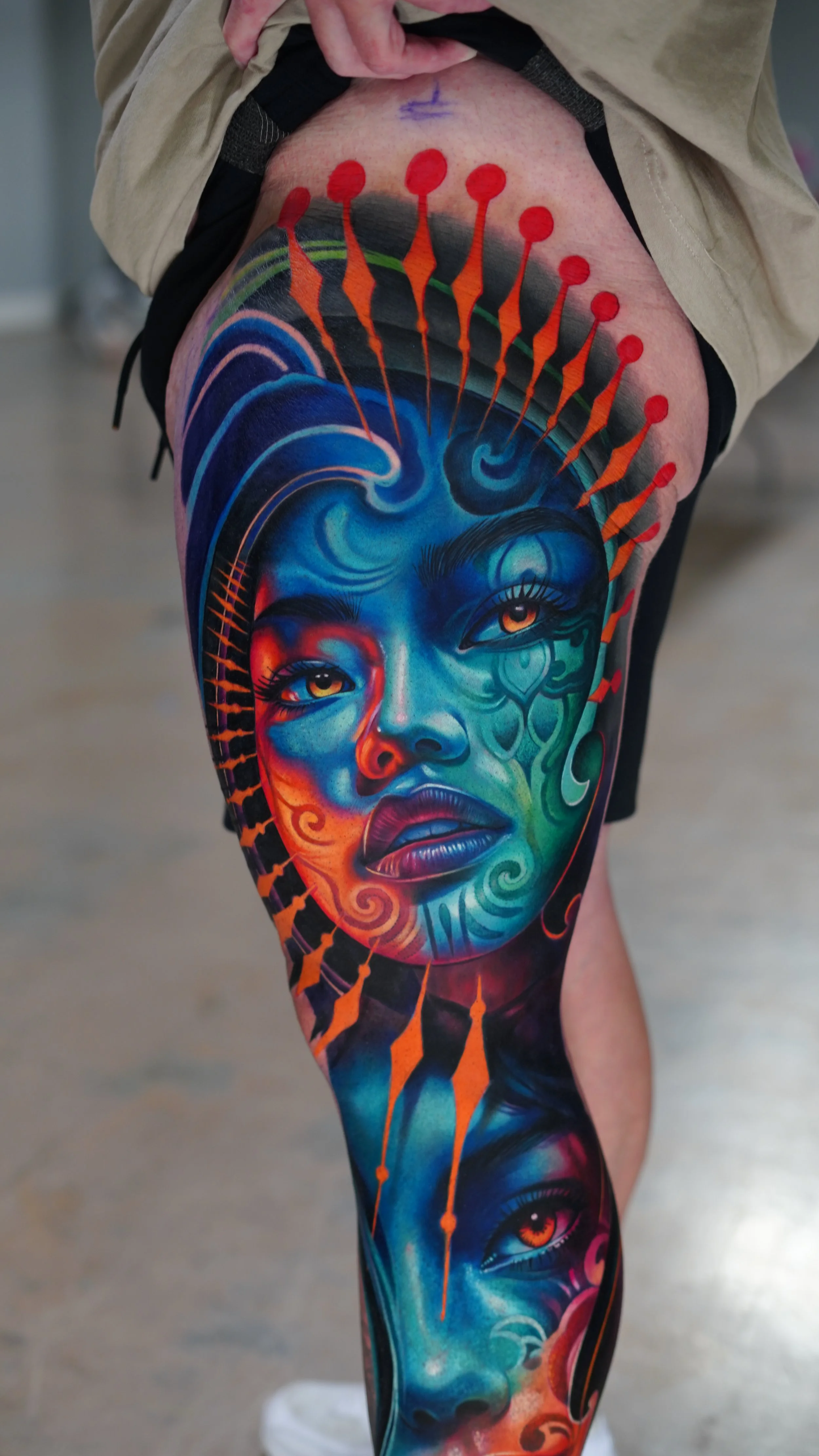 Colorful tattoo of a woman's face with vivid blues, oranges, and greens covering the person’s thigh and calf.