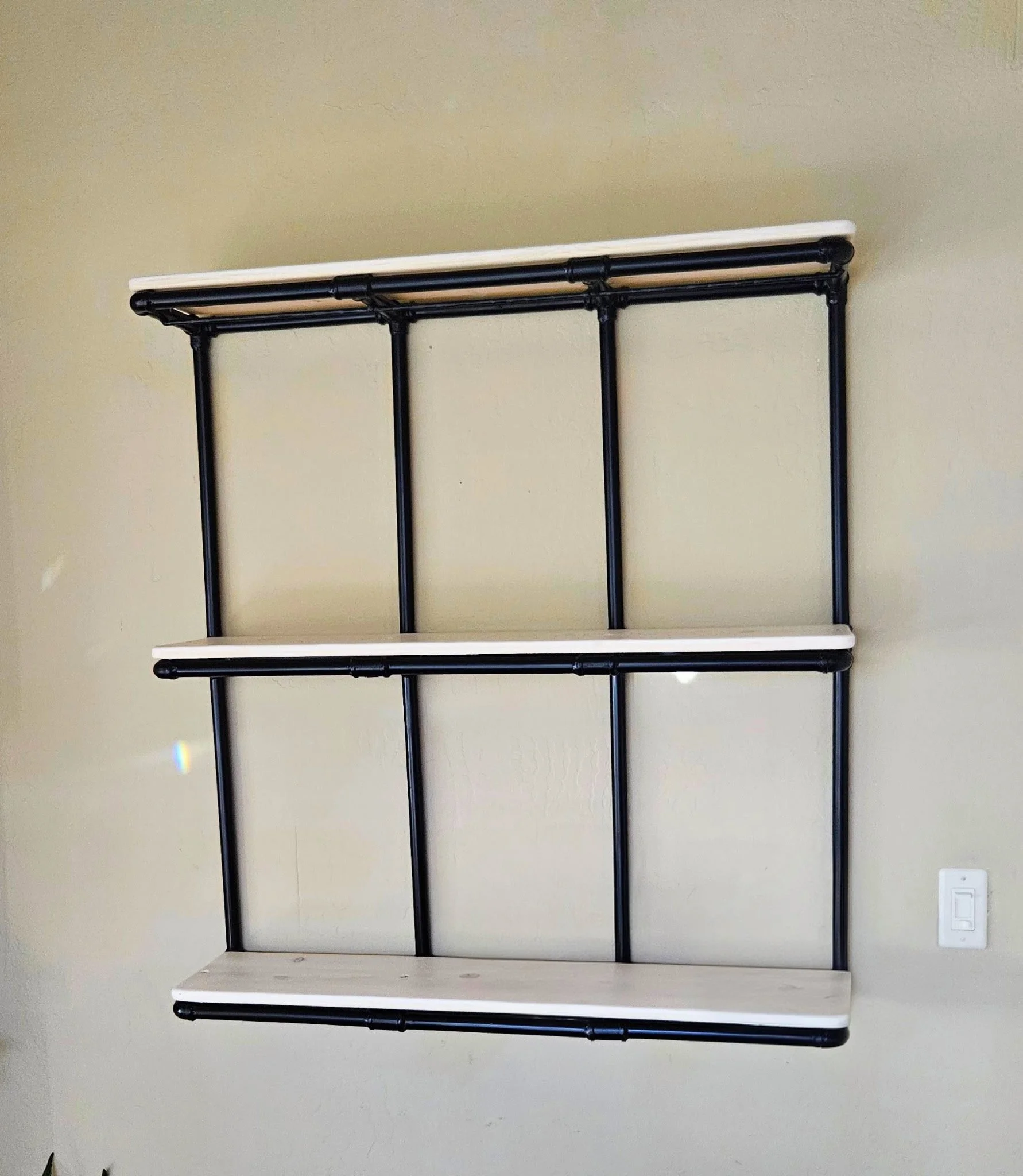 Wall-mounted shelving unit with three empty wooden shelves supported by black metal pipe brackets.