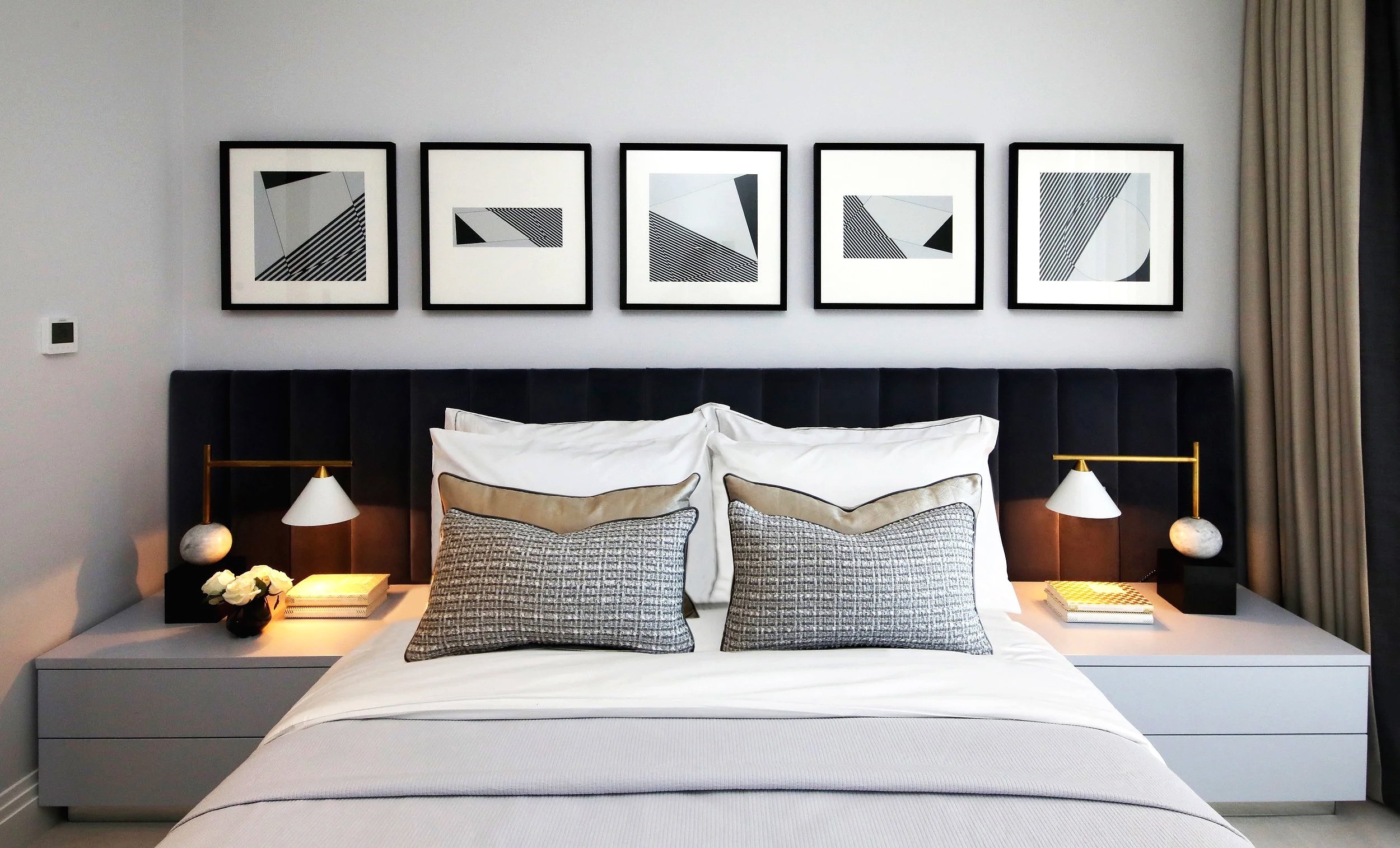 Modern luxury bedroom with white linens, decorative cushions, nightstands with Kelly Wearstler lamps, and black-and-white abstract wall art