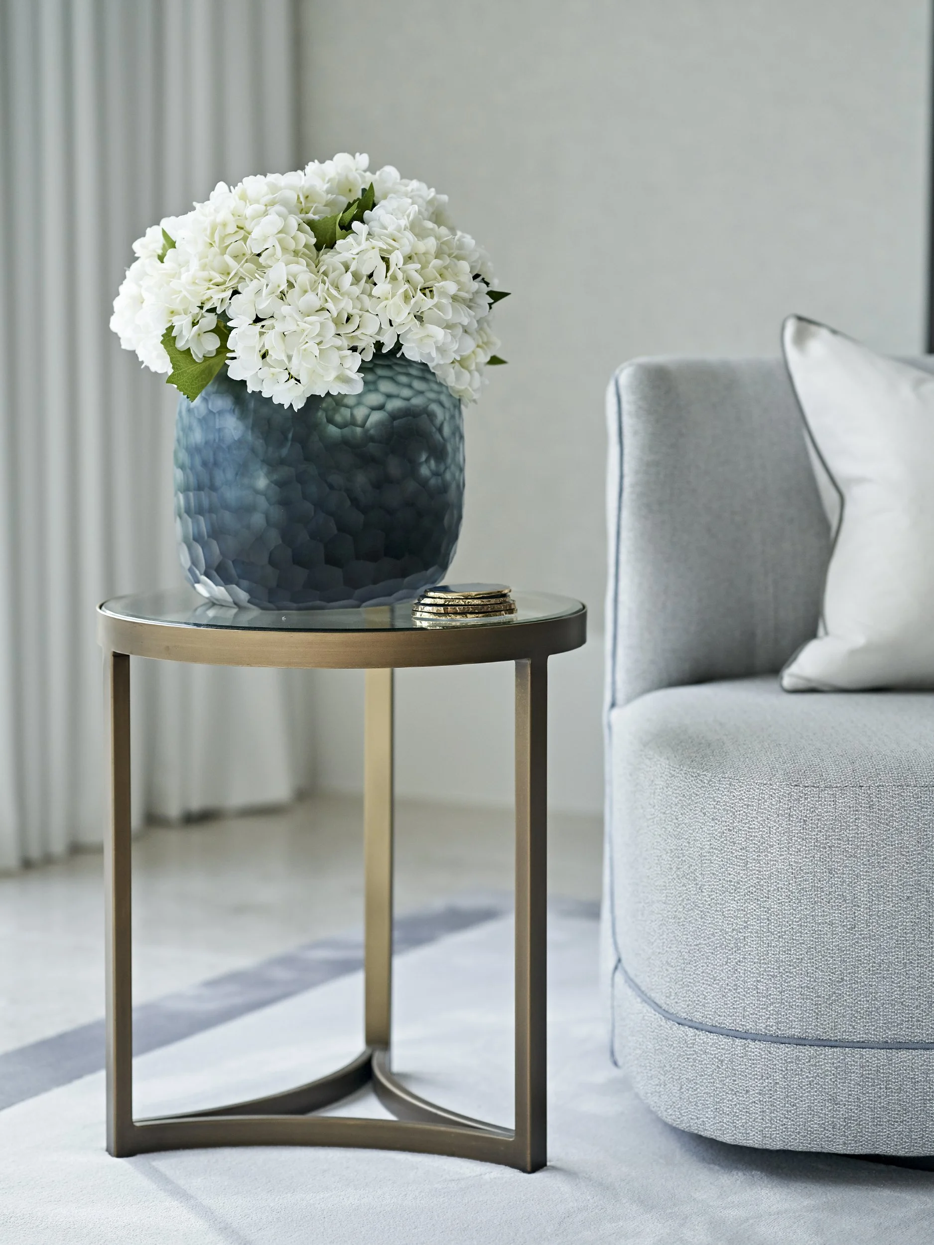 Modern luxury living room with light sofa and side table styled with textured blue vase of white hydrangeas