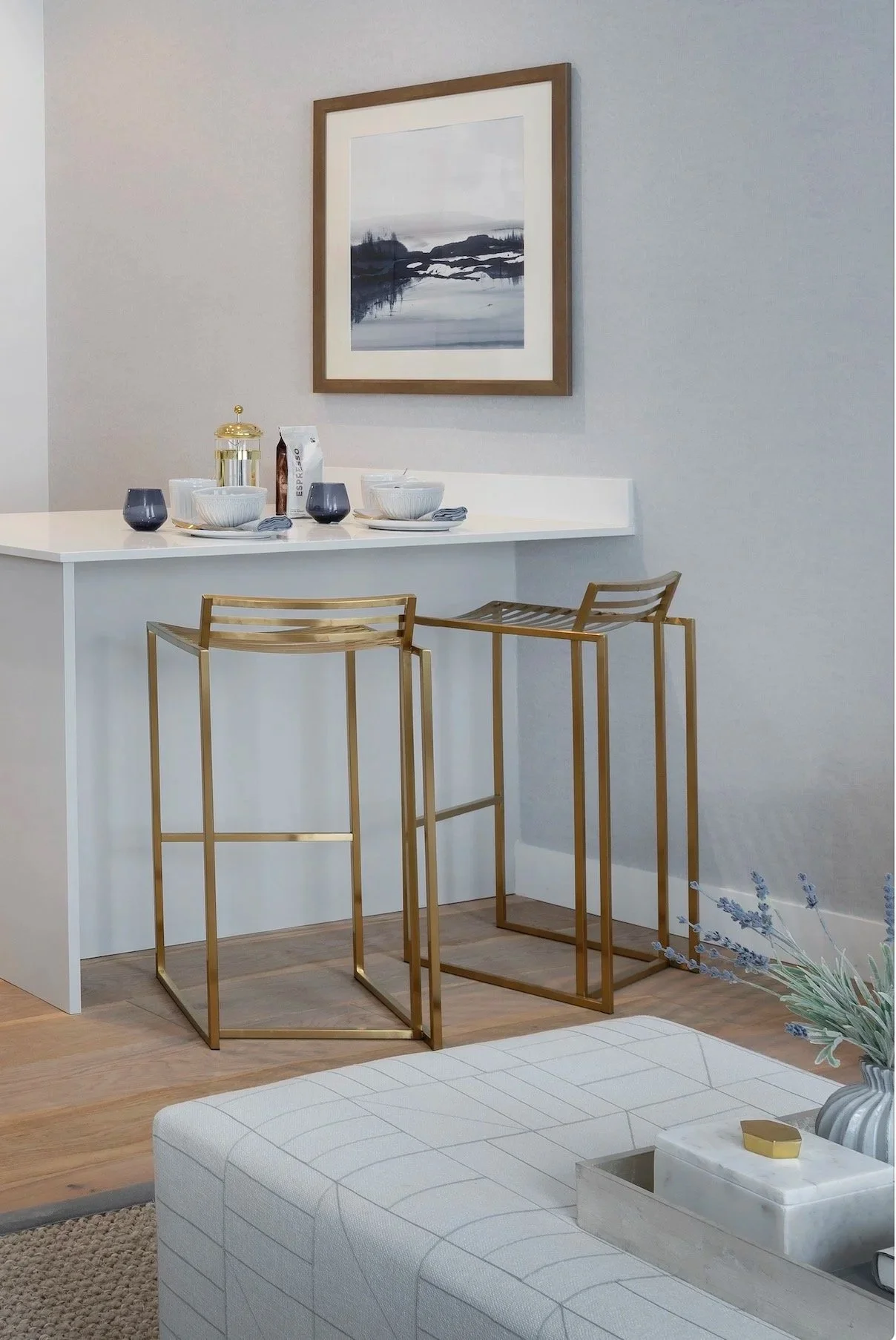 Modern coastal kitchen with island, gold bar stools, geometric ottoman, black and white artwork, and decorative accessories
