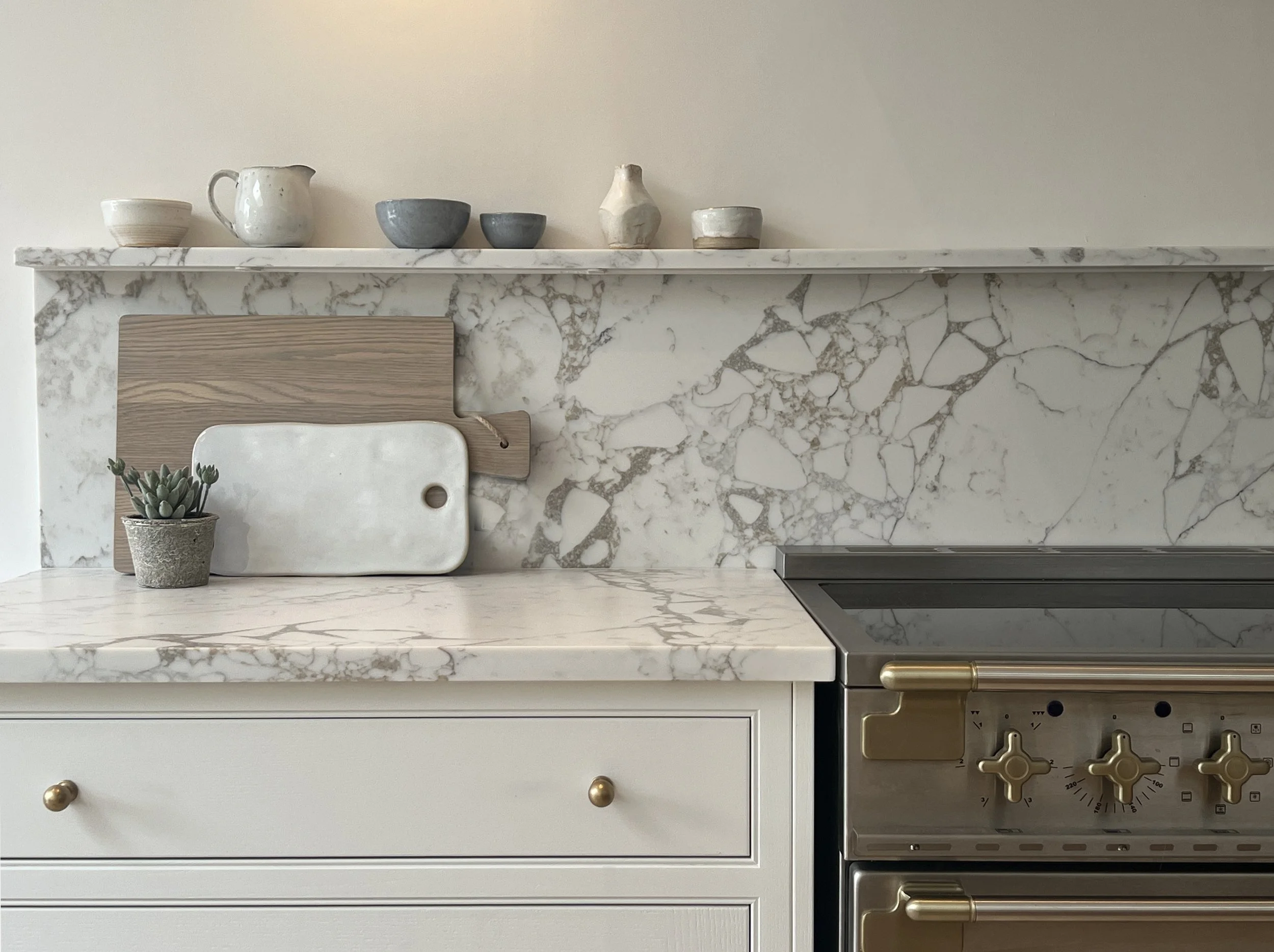 Modern luxury classic shaker kitchen with white marble surfaces, gold-accented range cooker, styled with decorative accessories.