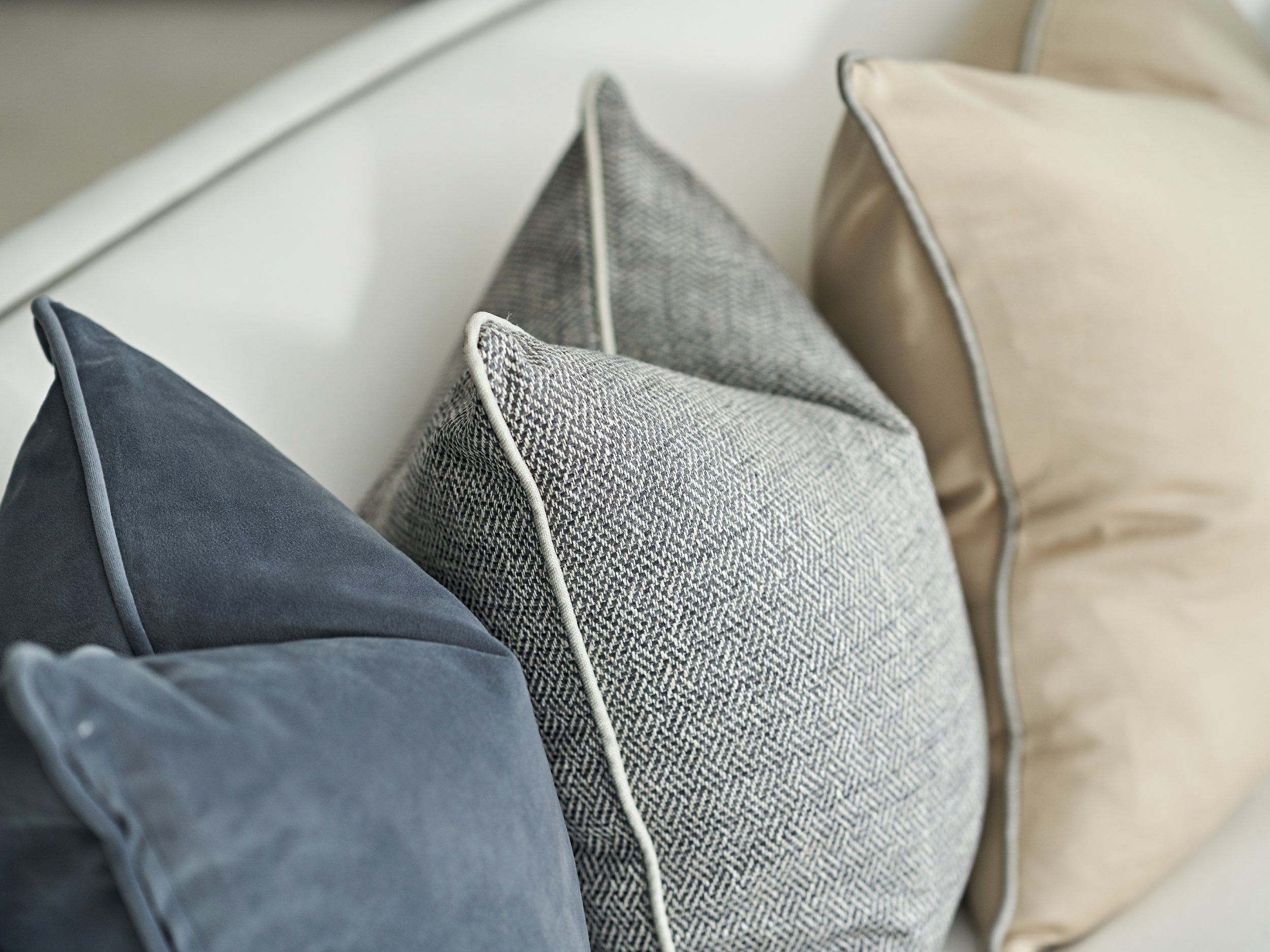 Decorative cushions on white sofa: petrol blue, blue textured with white piping, and soft gold with grey piping — modern luxury living room styling.