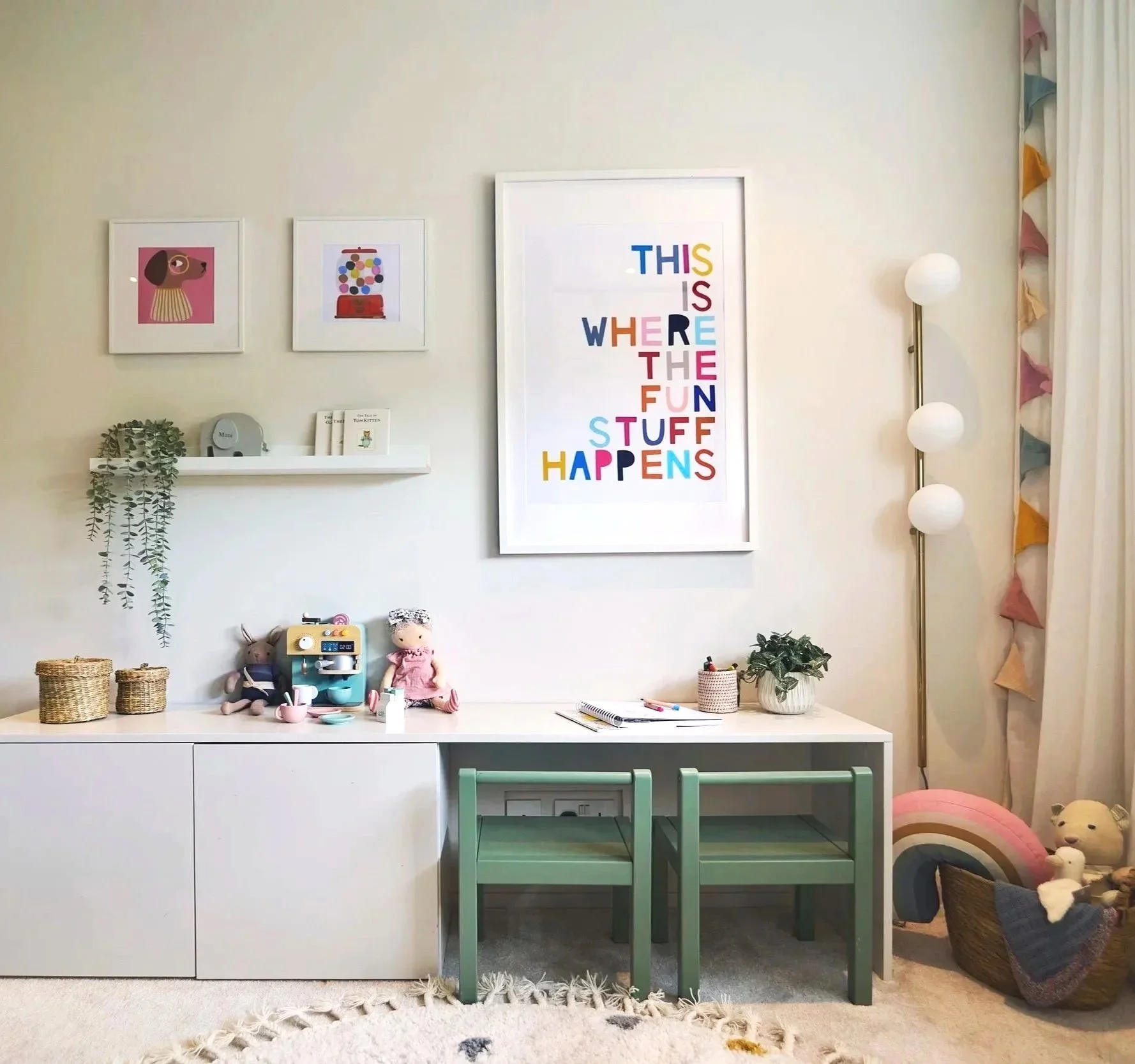 Modern kids’ bedroom with built-in desk, colorful wall art, shelf with toys and plants, and playful wall light and bunting.