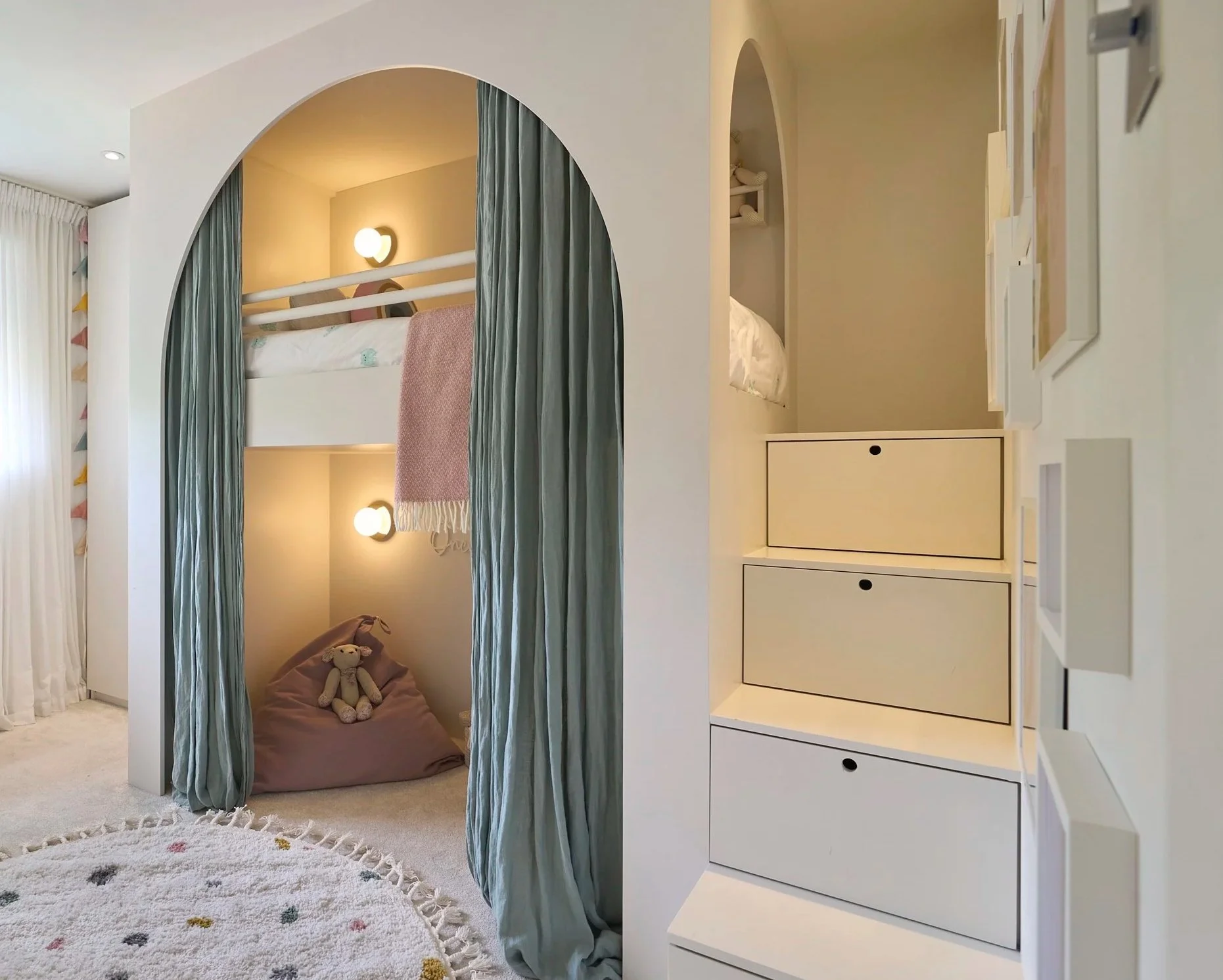 Modern children’s bedroom with built-in bunk bed and play den, linen curtains, colorful wall art, and storage steps.
