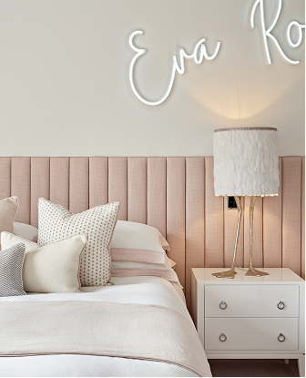Luxury child’s bedroom with pink headboard, decorative cushions, white bedside table, feathered lamp, and neon sign on wall