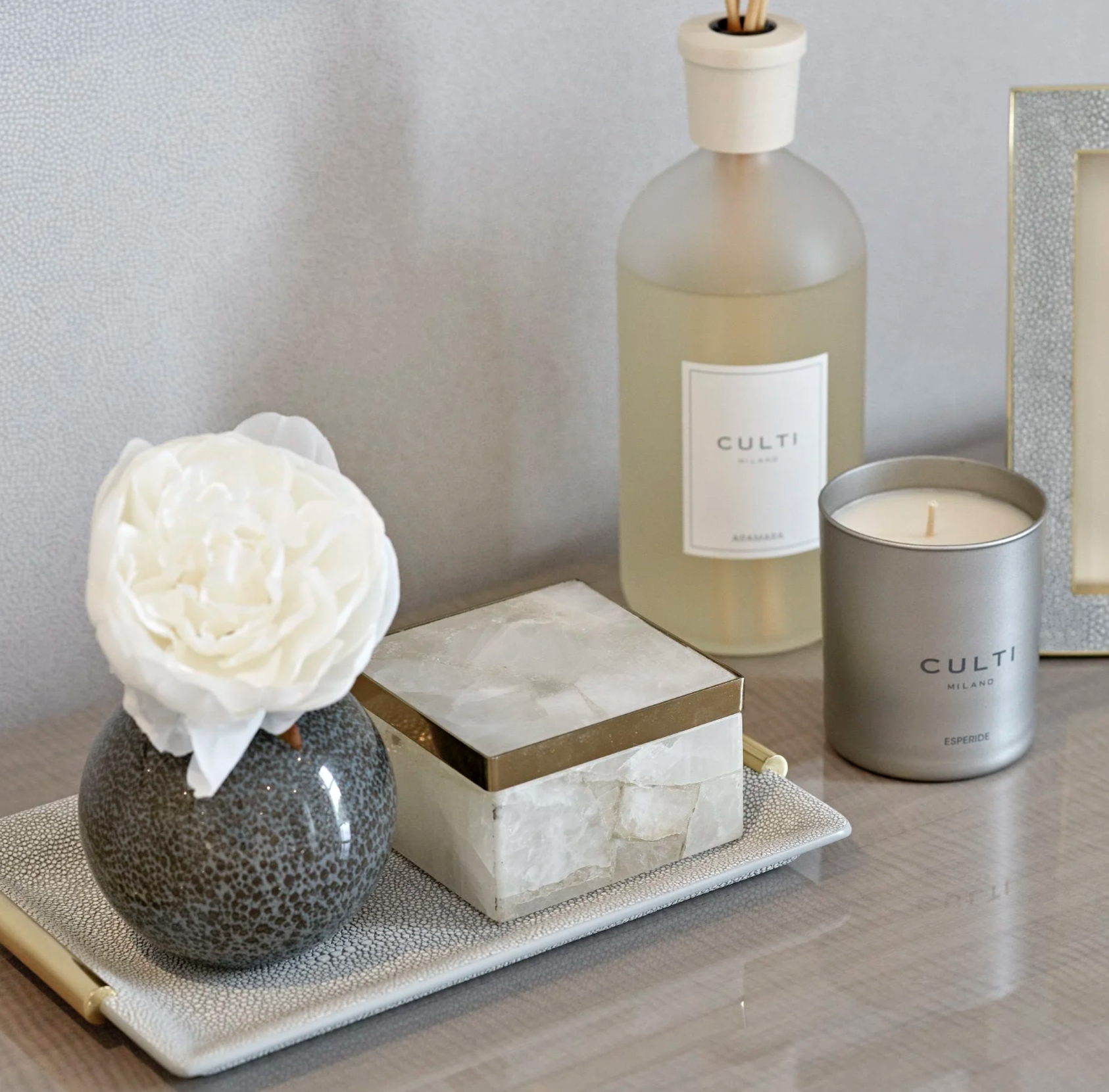 Luxury table styling with grey glass vase, white peony, agate box, frosted diffuser, silver candle, and shagreen picture frame.