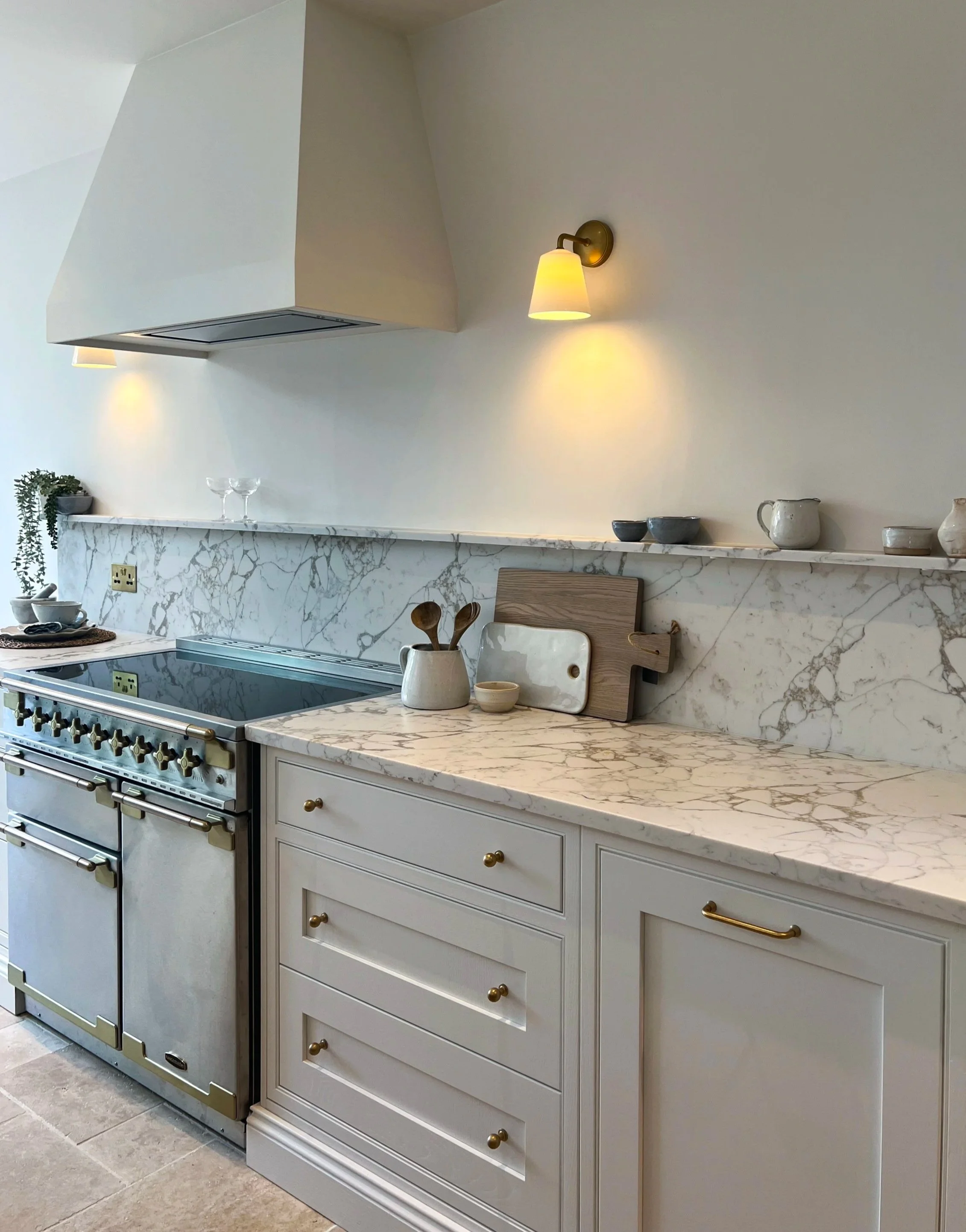 Modern luxury shaker kitchen featuring white marble surfaces, gold-accented range cooker, and brass wall lights & ceramic accessories