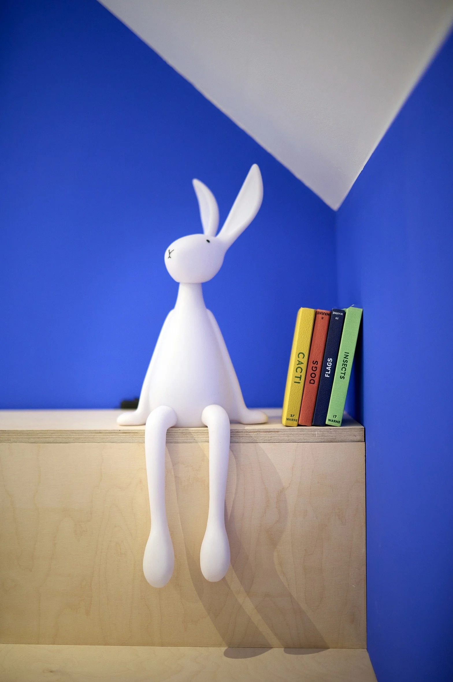 Kids’ bedroom detail with white rabbit lamp on wooden bunk bed steps, colorful books, and blue accent wall.
