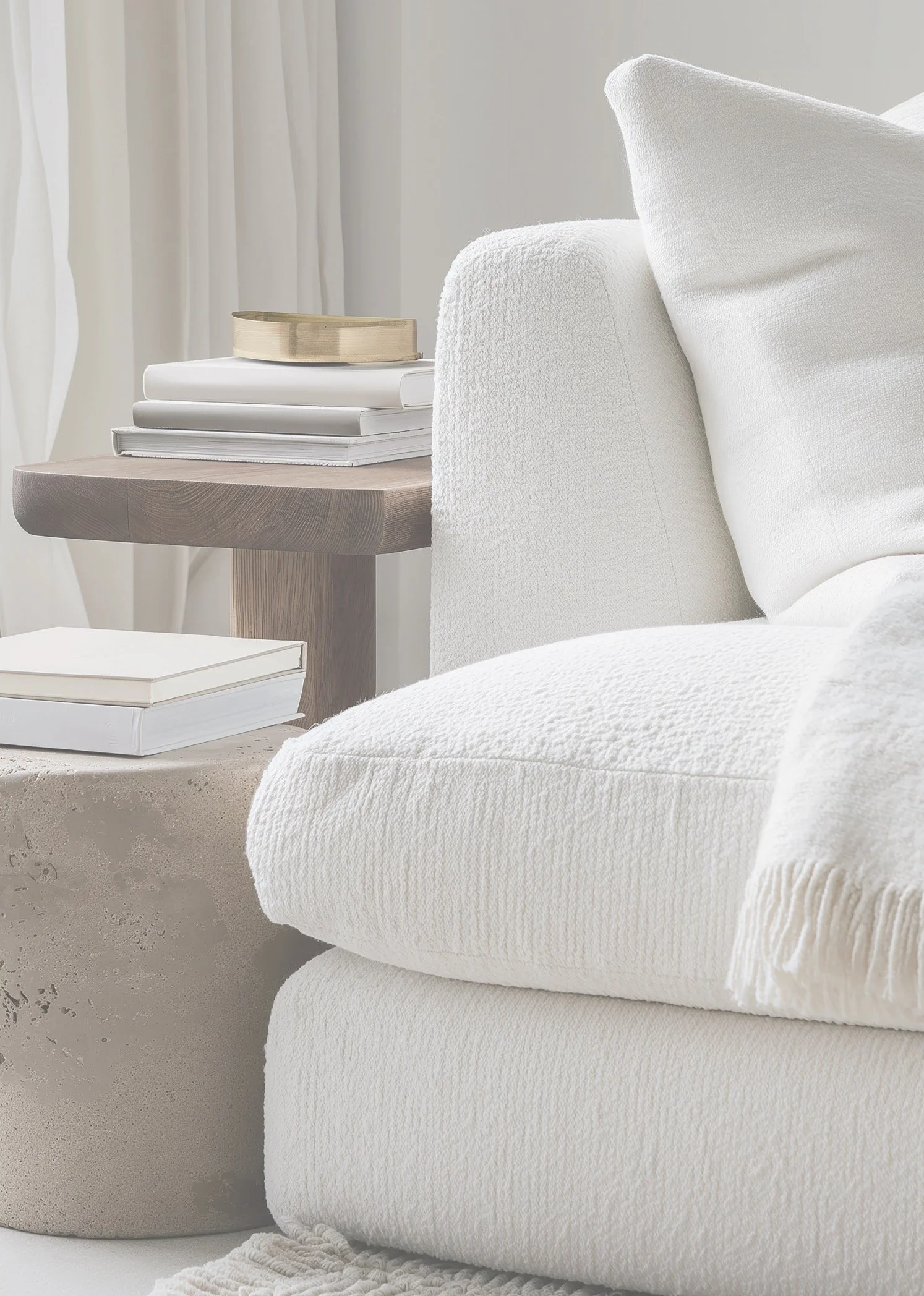 White boucle sofa and stone side table with books in a bright neutral room