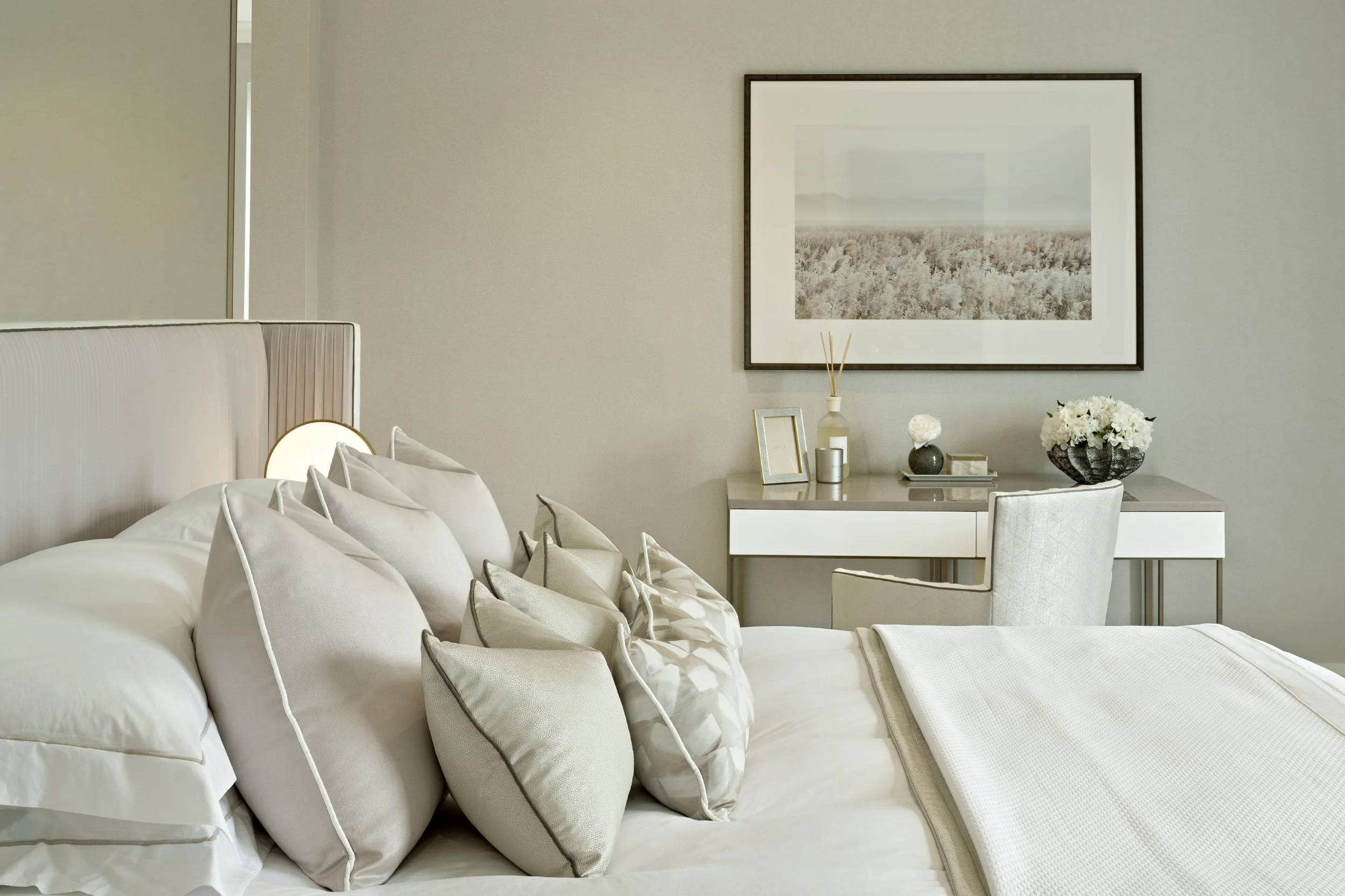 Modern luxury bedroom featuring pleated headboard, layered cushions, bedside lamp, and contemporary desk with decorative accessories