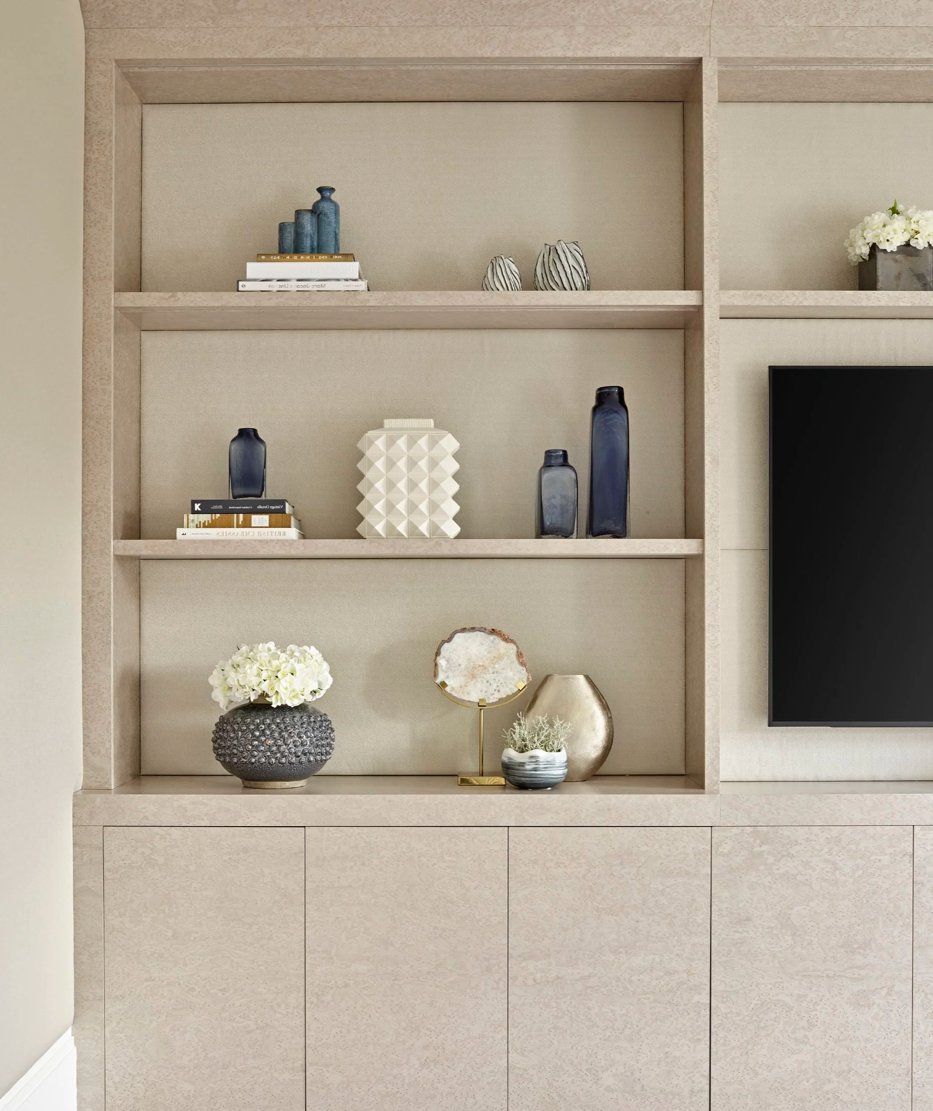 Decorative pale birch TV joinery with cupboards and shelves, styled with books, vases, and gold, blue, and white accents in a modern TV den