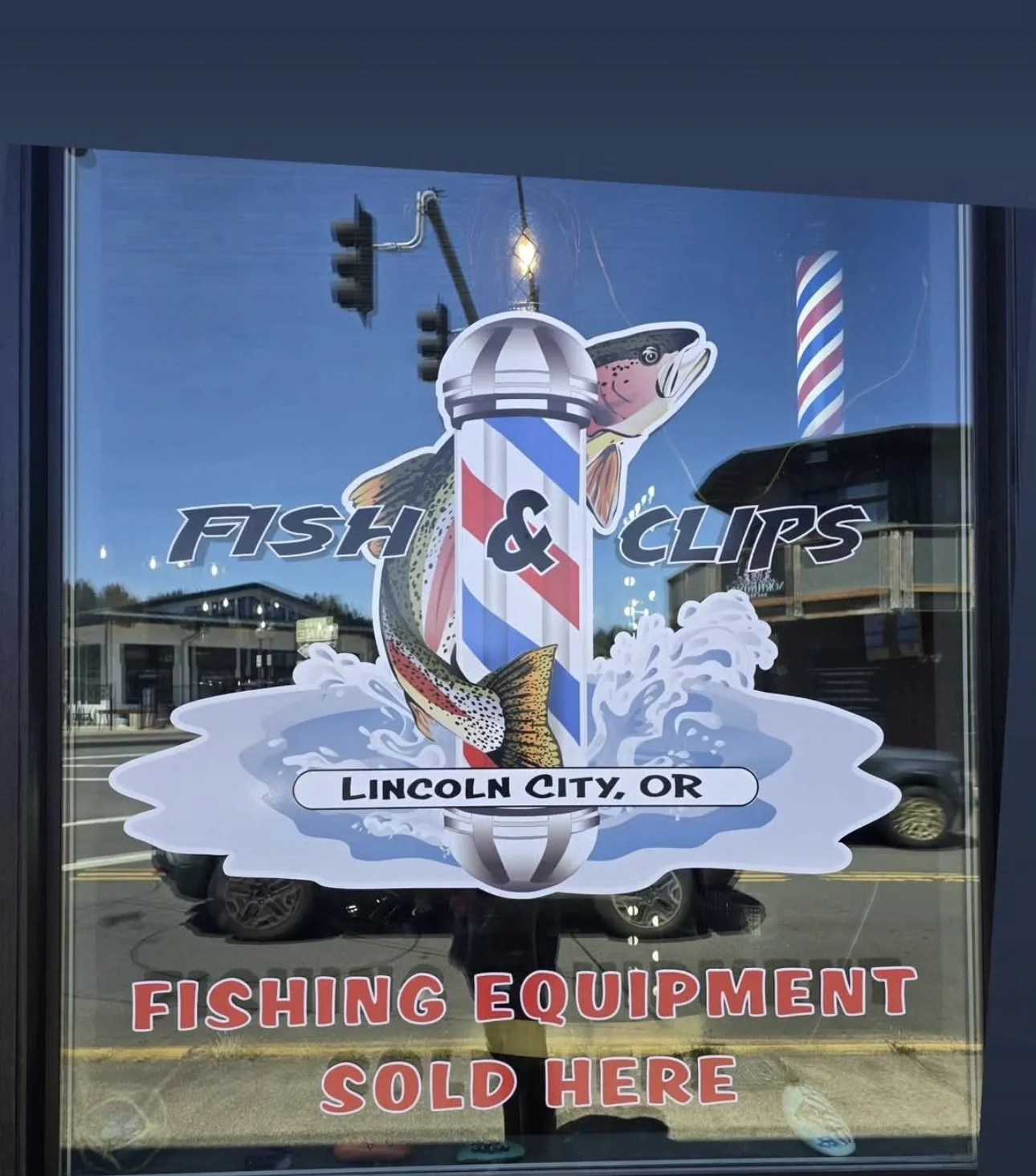 Sign on shop window for Fish & Clips, Lincoln City, OR. Features an illustration of a fish, a barber pole, and water splash, advertising fishing equipment for sale.