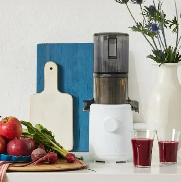Hurom slow juicer on a kitchen counter with two glasses of fresh red beet juice, surrounded by apples, beets, and leafy greens.