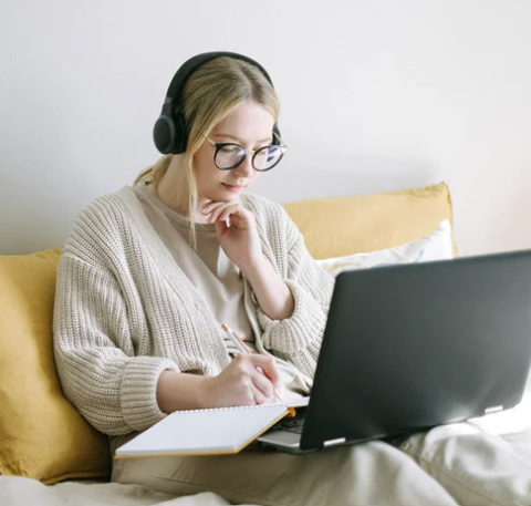 A clinician wearing headphones takes notes while watching an online training on her laptop.