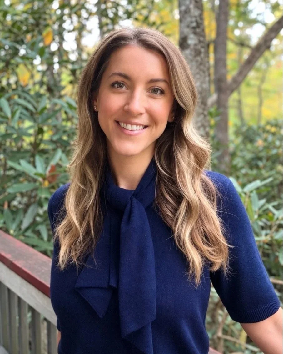 Professional portrait of Kristen Hamilton the founder and clinical director of the luminary group: smiling woman in a navy blue top with long, wavy brown hair in an outdoor woodland setting.