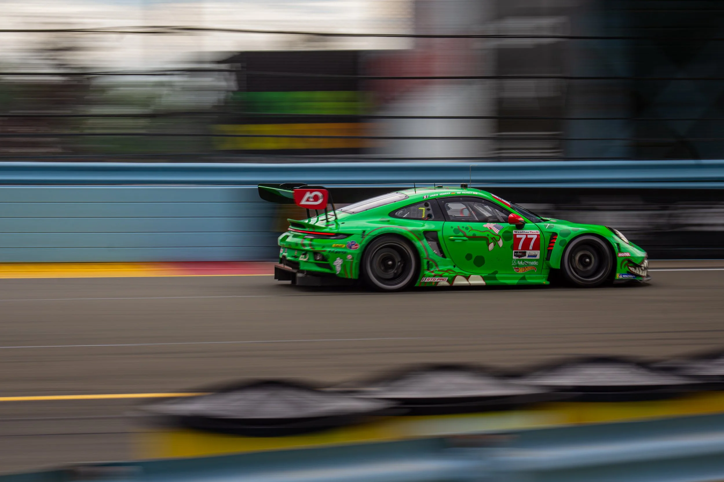Green race car with colorful graphics speeding on a racetrack, with blurred background and motion blur.
