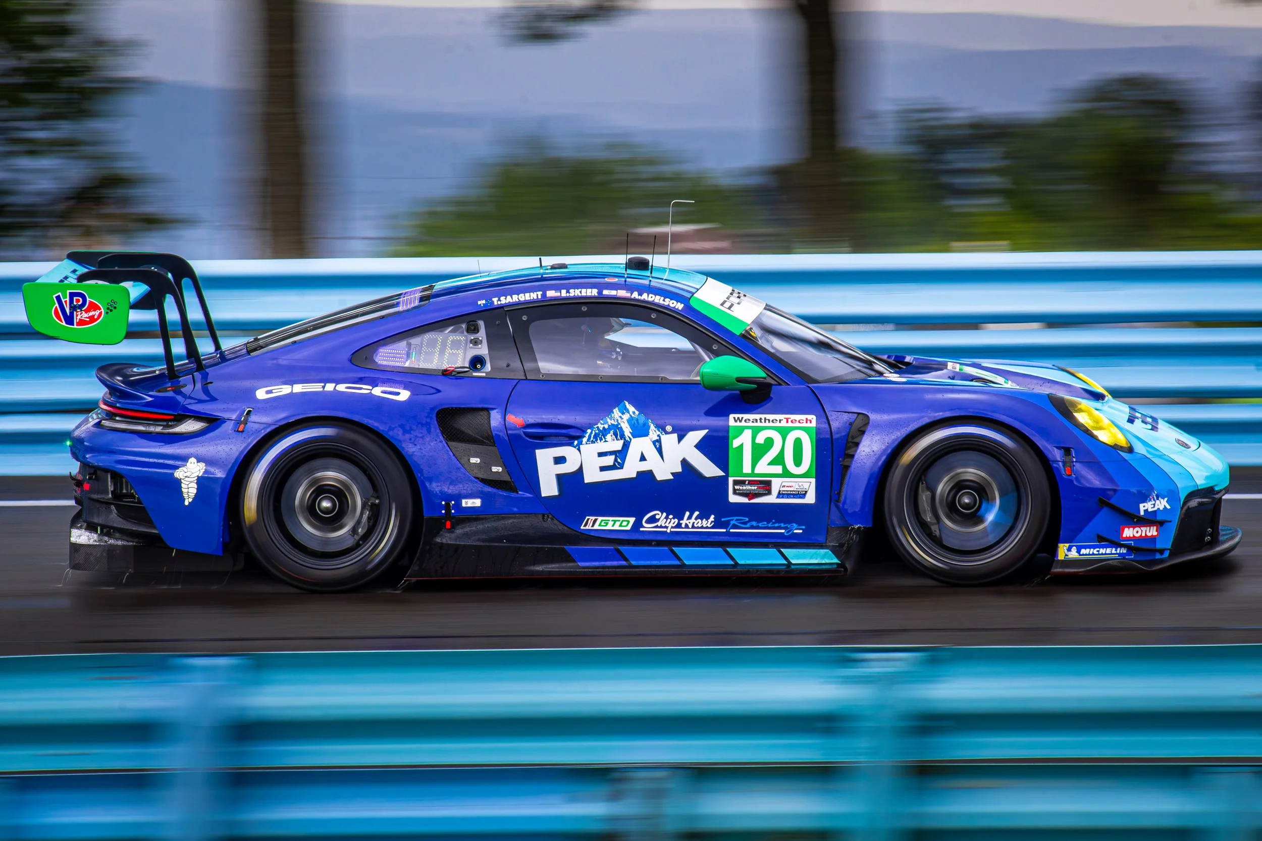 A blue race car with sponsorship stickers moving on a racetrack, displaying a rear wing, race number 120, and a driver inside.