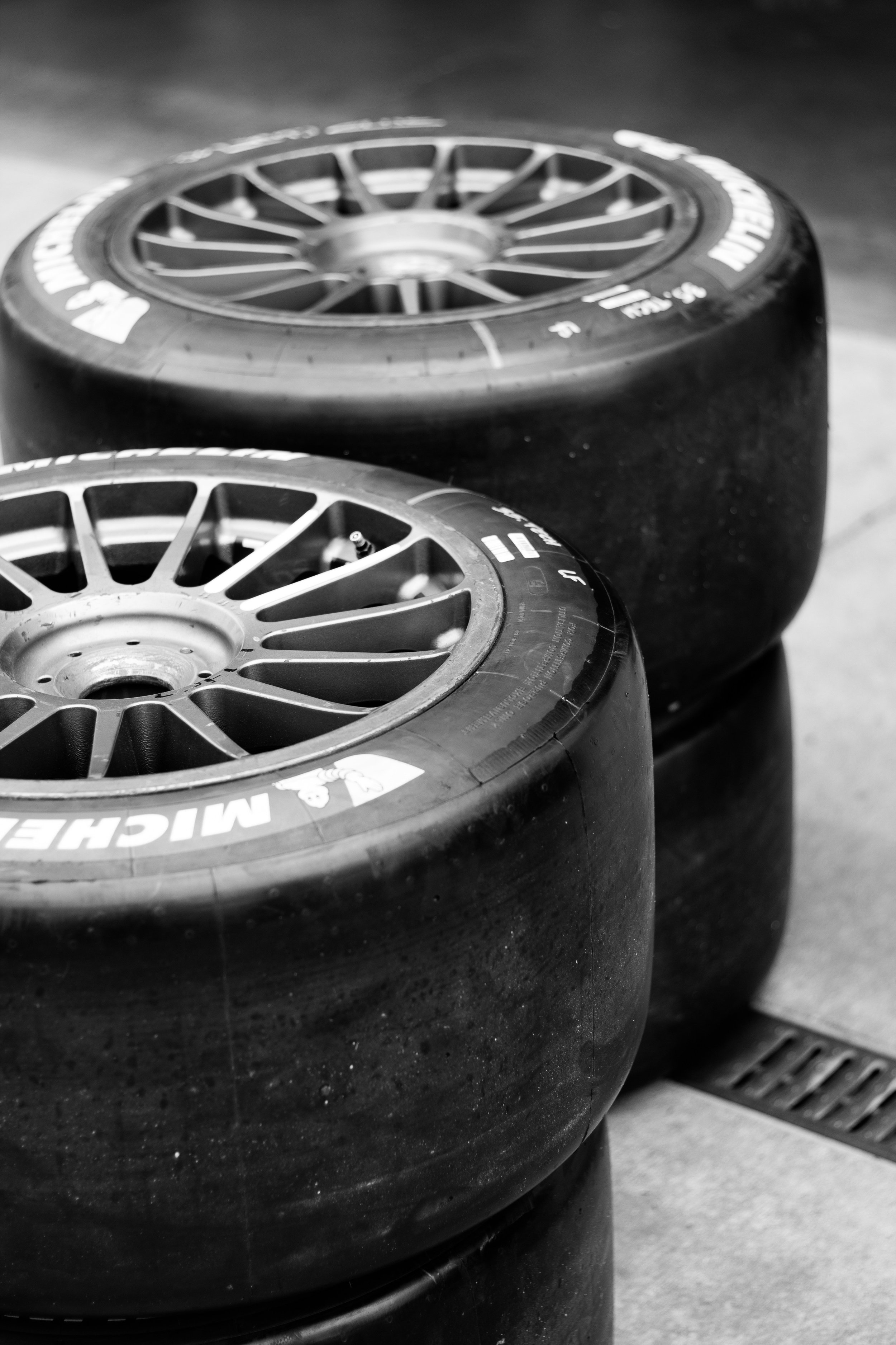 Two racing tires with alloy wheels stacked on a garage floor, black and white photo.