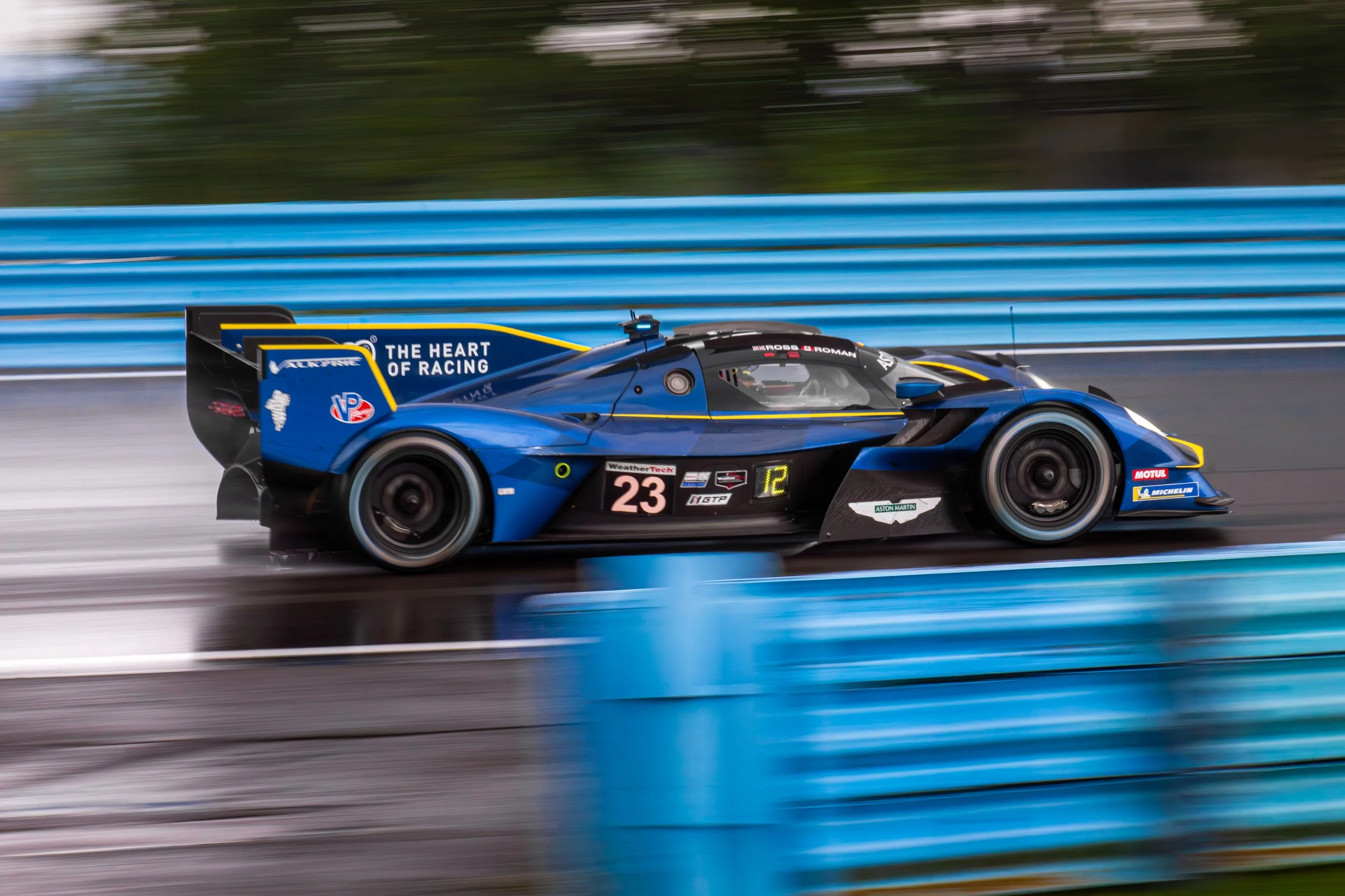 A blue race car moving at high speed on a racing track, with blurred blue barriers in the background.