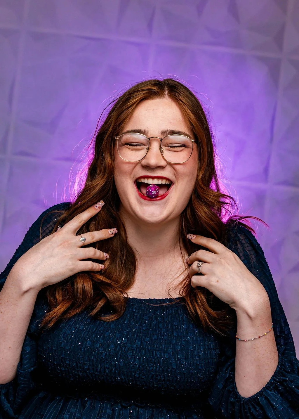 Headshot of Easlyn smiling at the camera and holding a D20 dice with her teeth