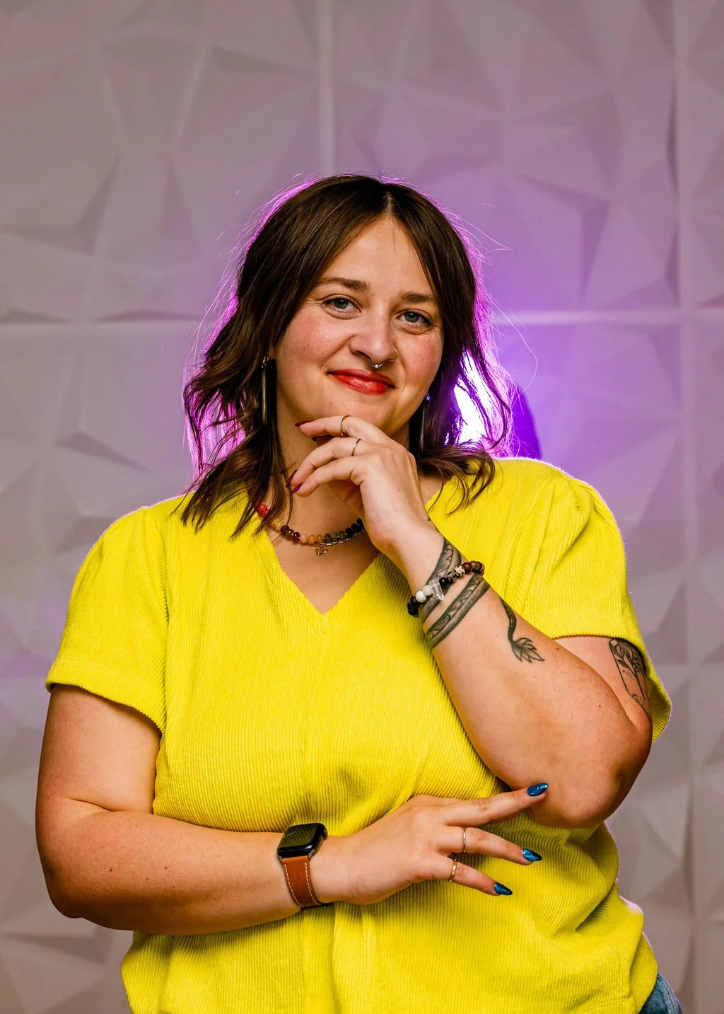 Headshot of Megan wearing a bright yellow shirt, smiling with hand on her chin