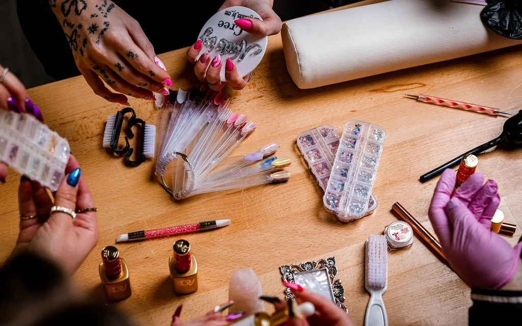 various nail art supplies on a table with nail tech hands working