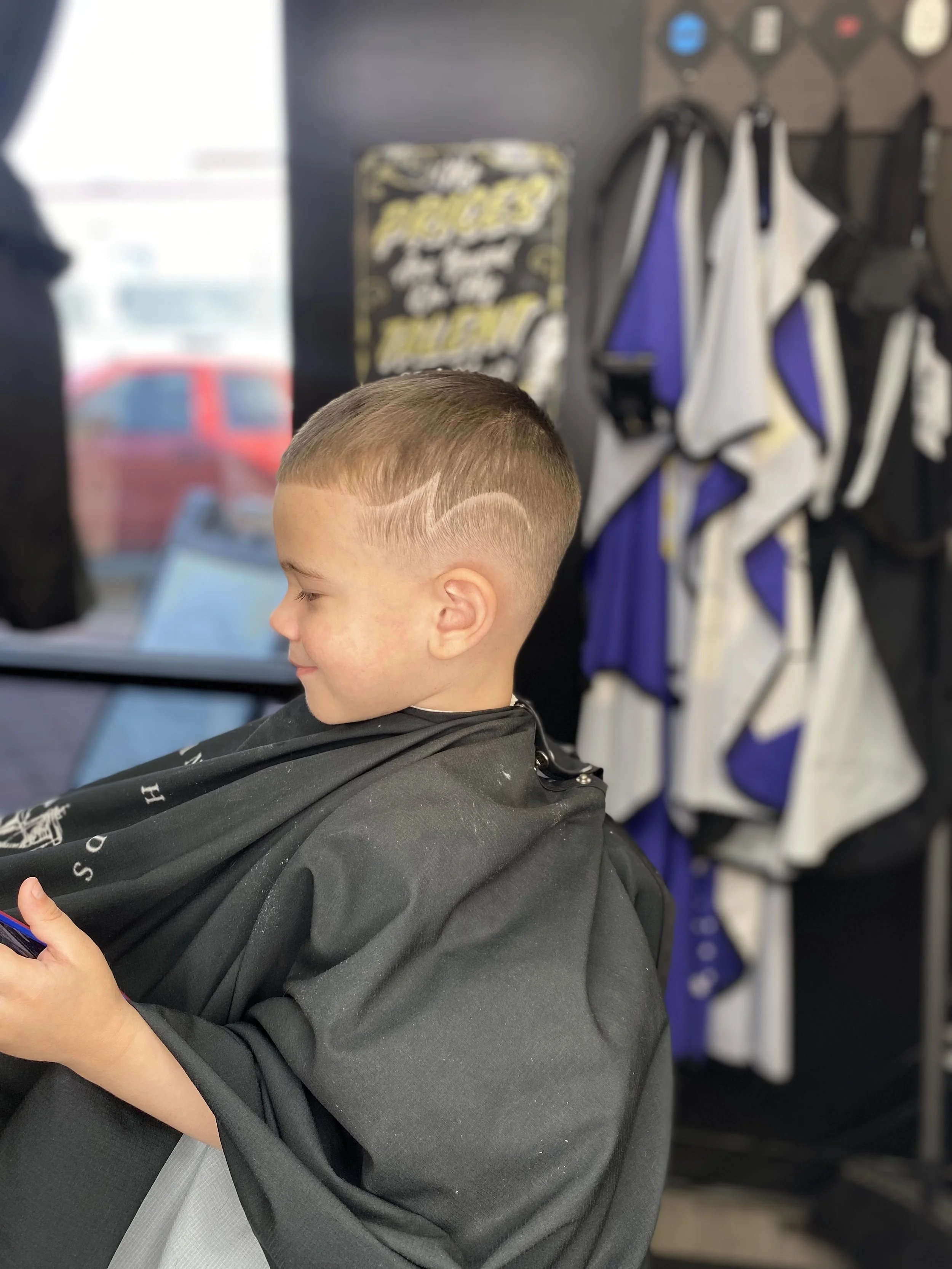 Young boy at a barbershop having a haircut, with fresh fade hairstyle featuring a curved line design on the side of his head.