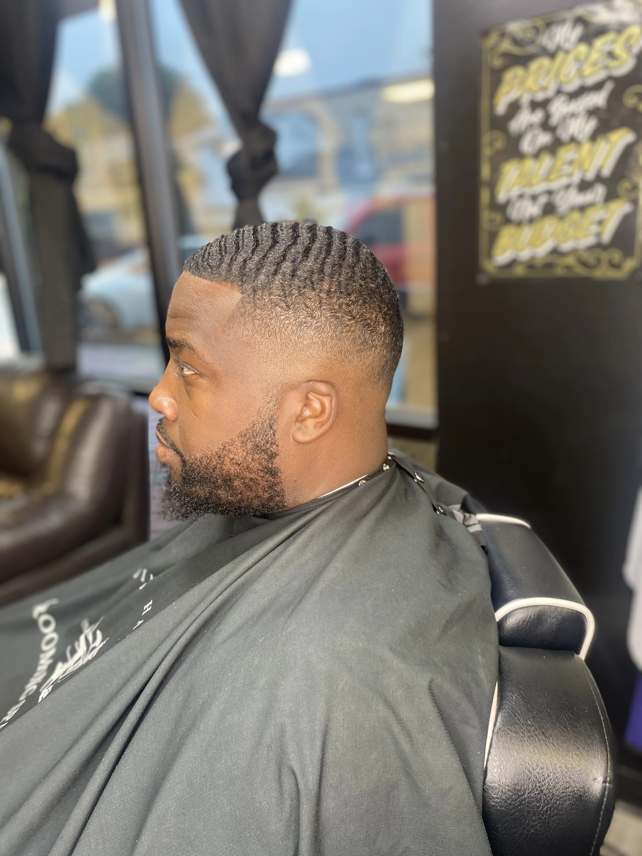 Close-up of a man with a fresh haircut featuring a fade and textured waves, sitting in a barber's chair in a barbershop.