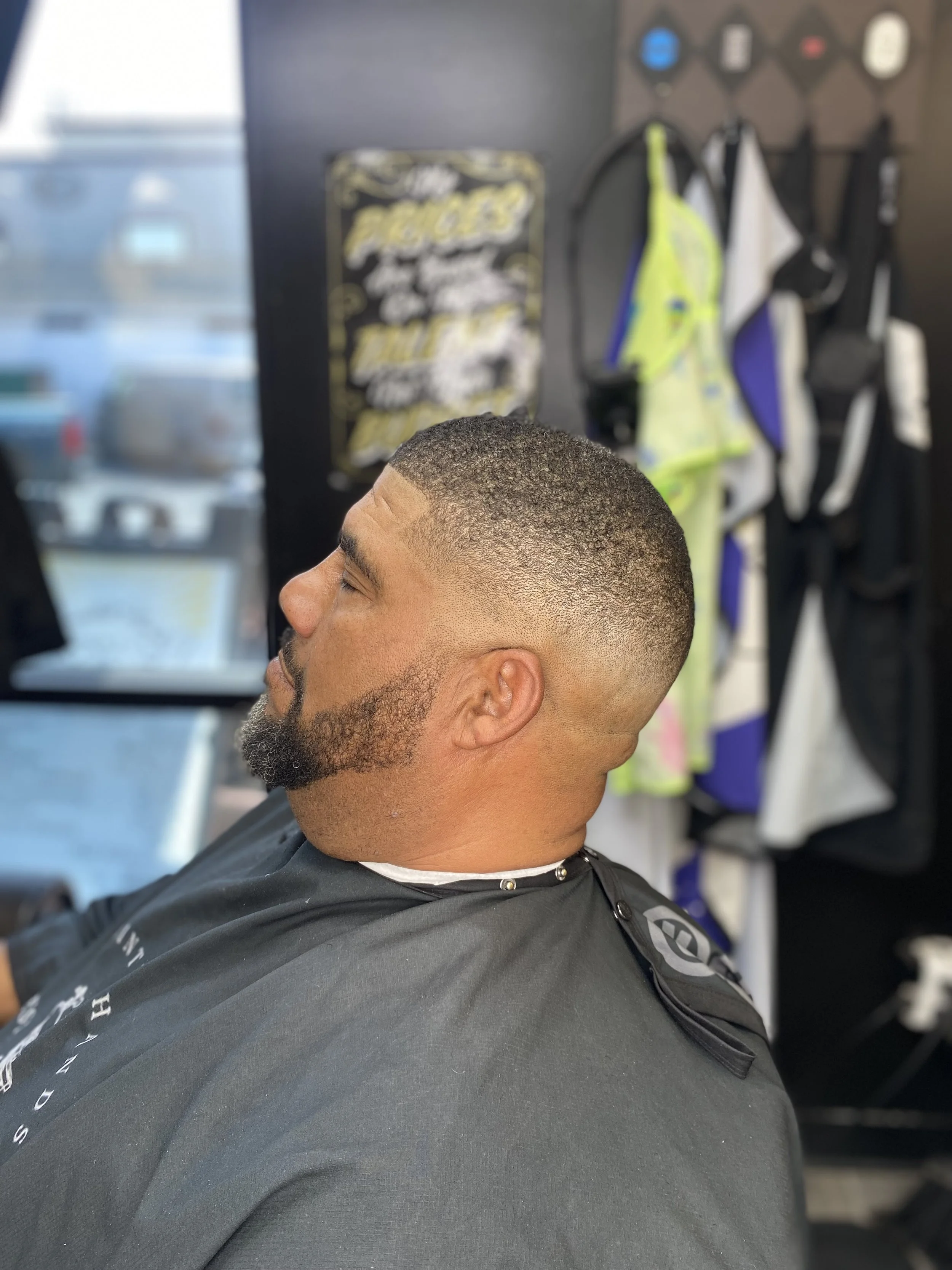 A man with a freshly cut short hairstyle and beard sitting in a barber shop chair.