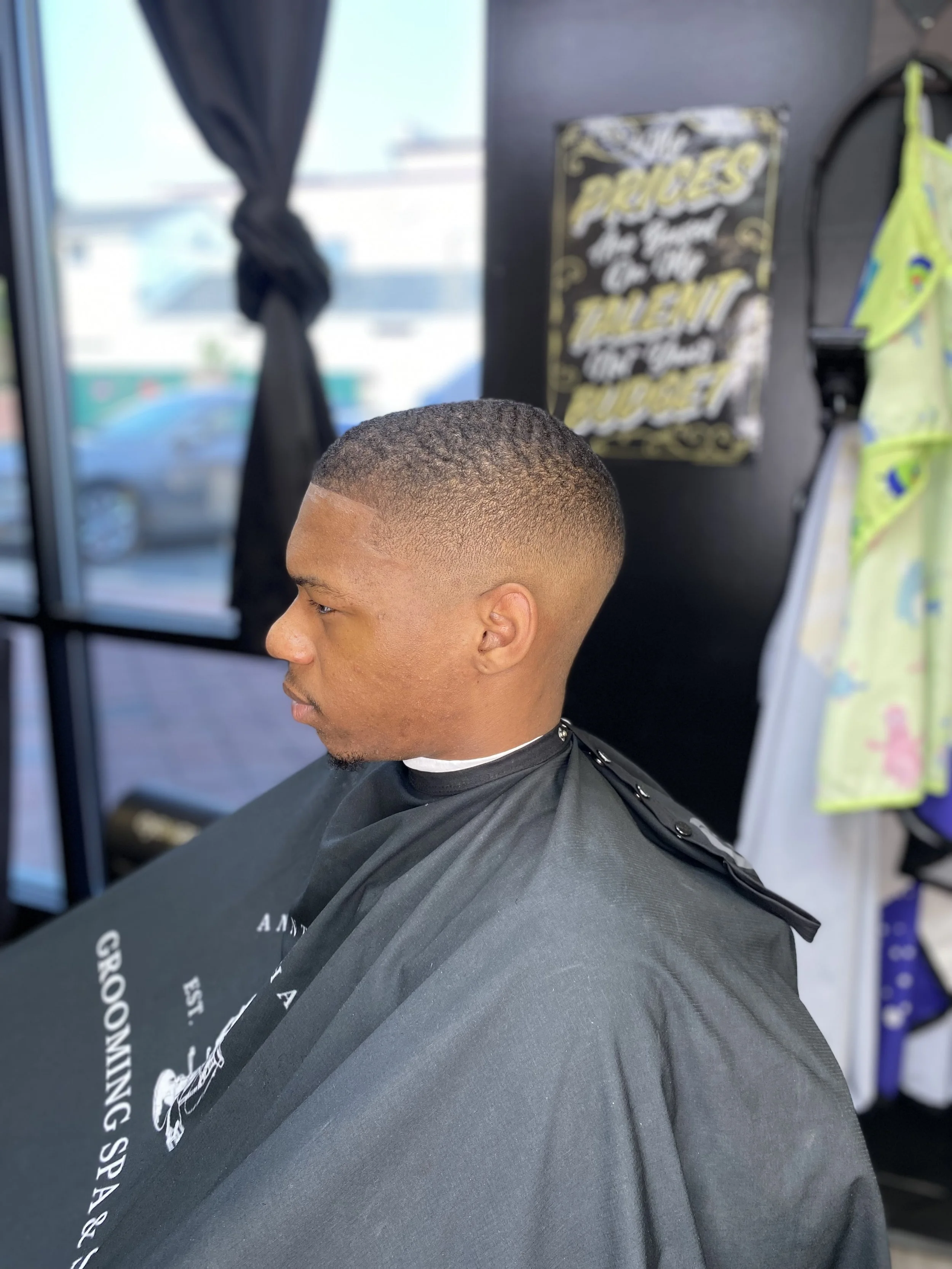 A man with a freshly cut fade hairstyle sitting in a barber's chair at a barbershop.